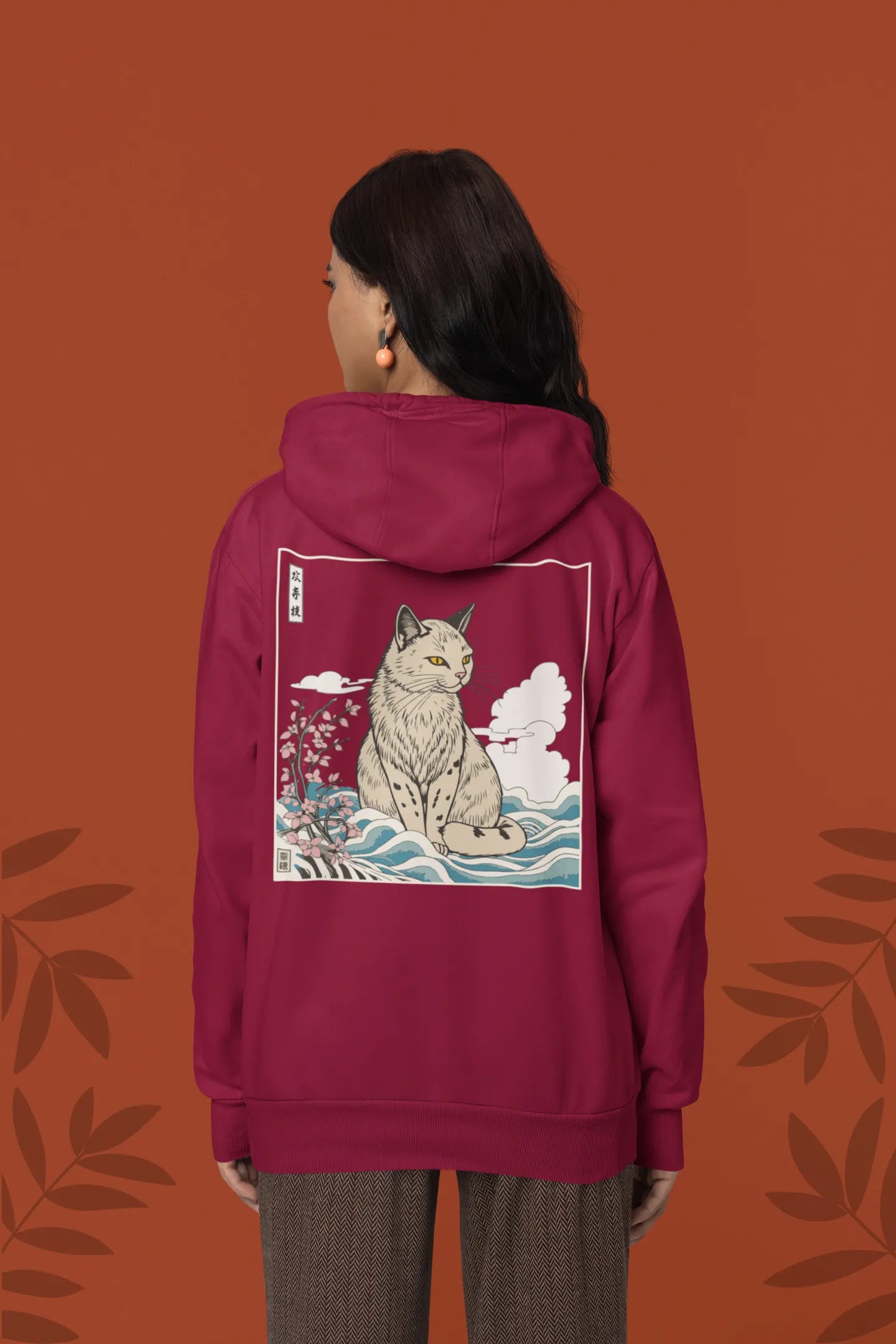 Back view of a female model wearing a maroon hoodie with a design of a wildcat sitting on ocean waves.