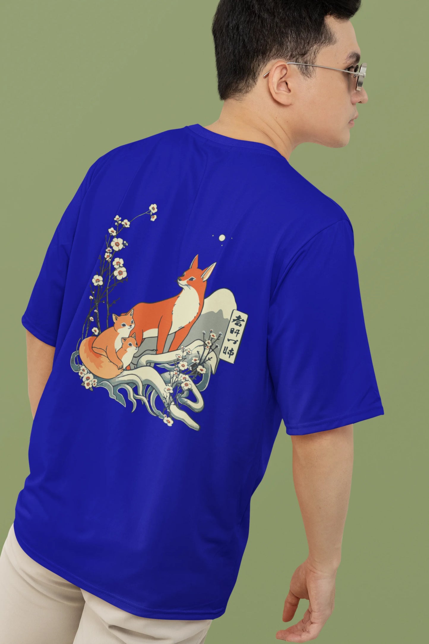 2nd back view of a male model wearing a royal blue oversized tee with a design of a fox and its cub in a traditional Japanese landscape.