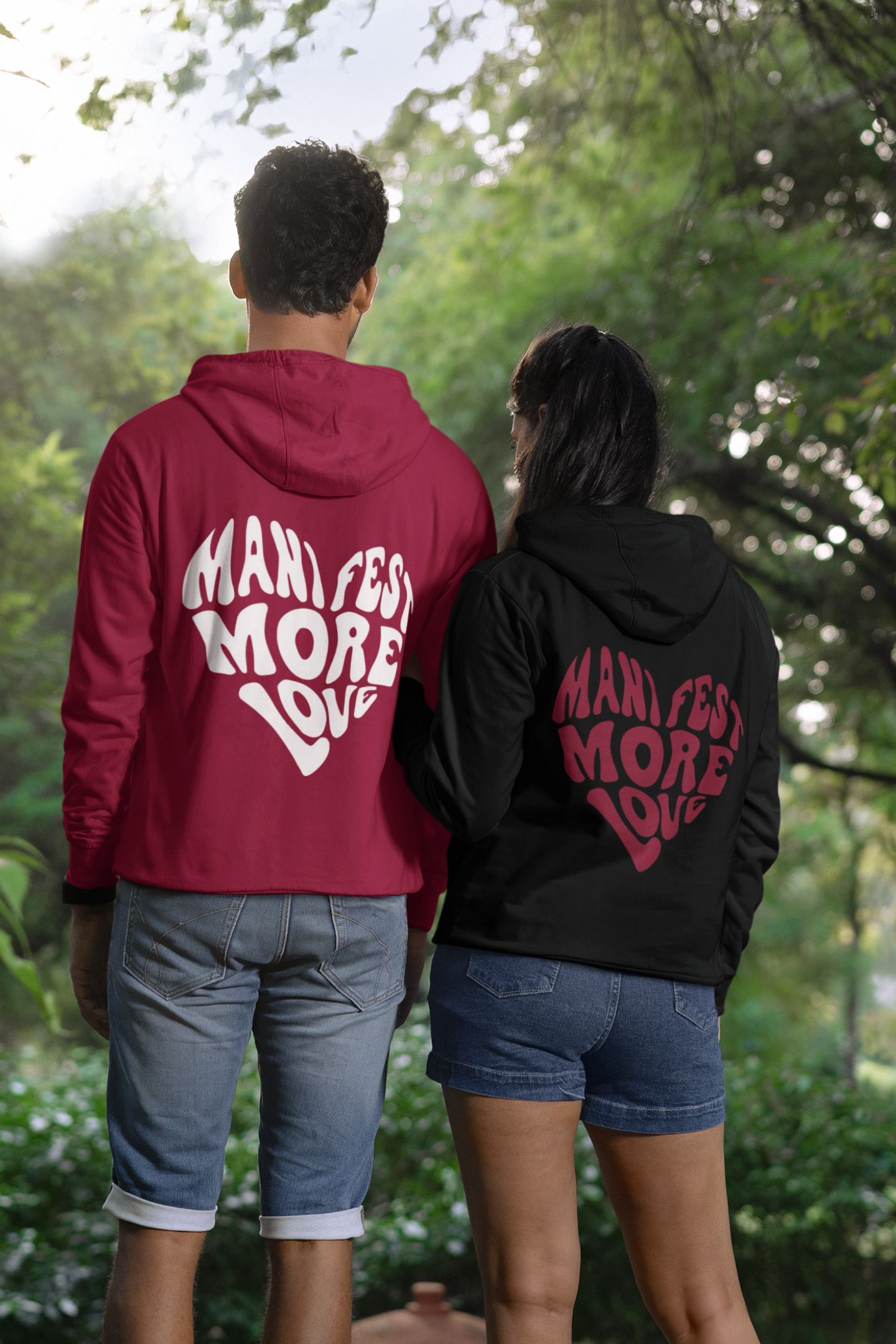 First back view of a couple wearing matching hoodies, each with a heart design containing the words "Manifest More Love."