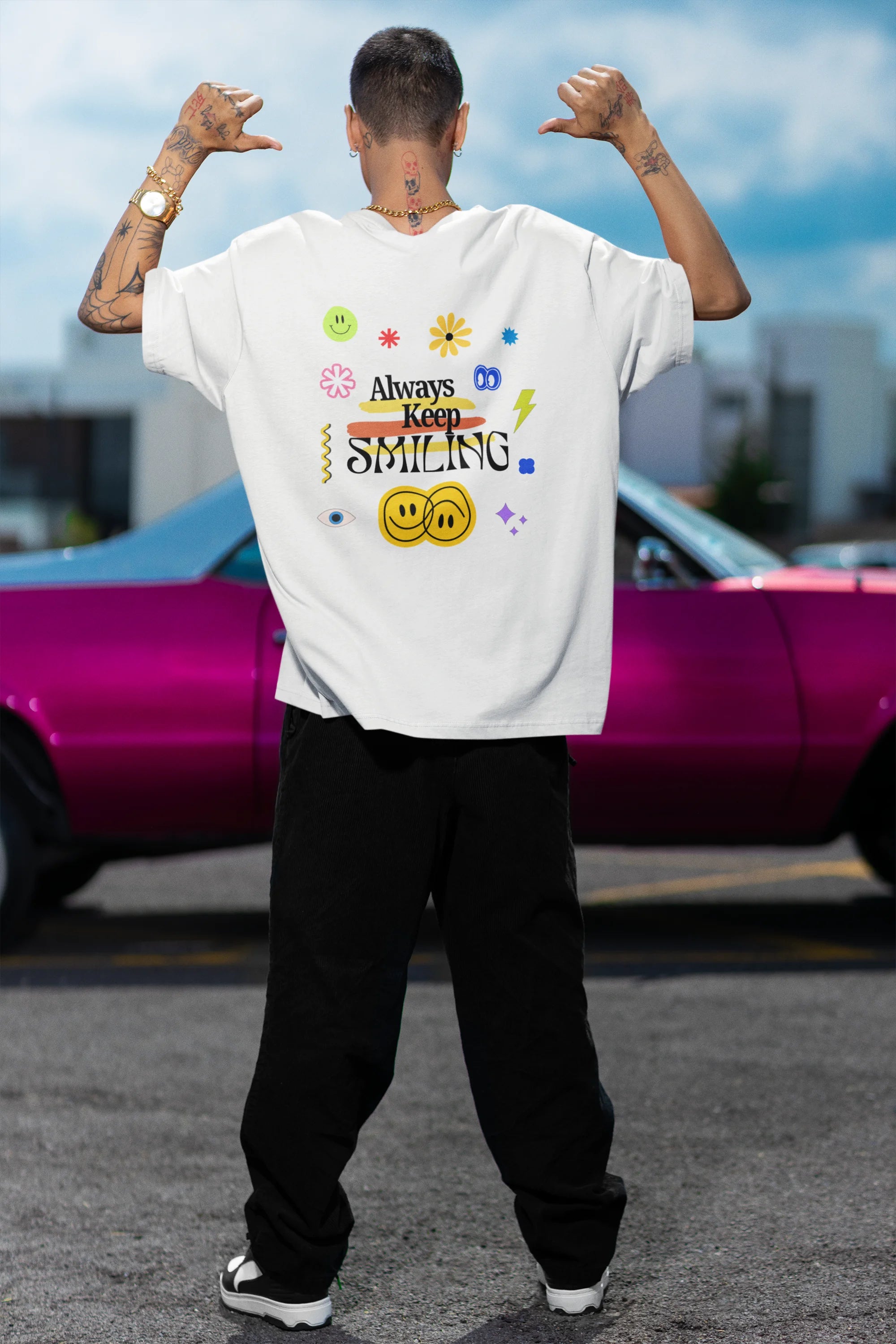 Back view of a male model wearing an oversized off-white t-shirt with a positive message "Keep Smiling" surrounded by colorful flowers and a smiley face emoji. Ideal for those who love cheerful clothing and spreading positivity.