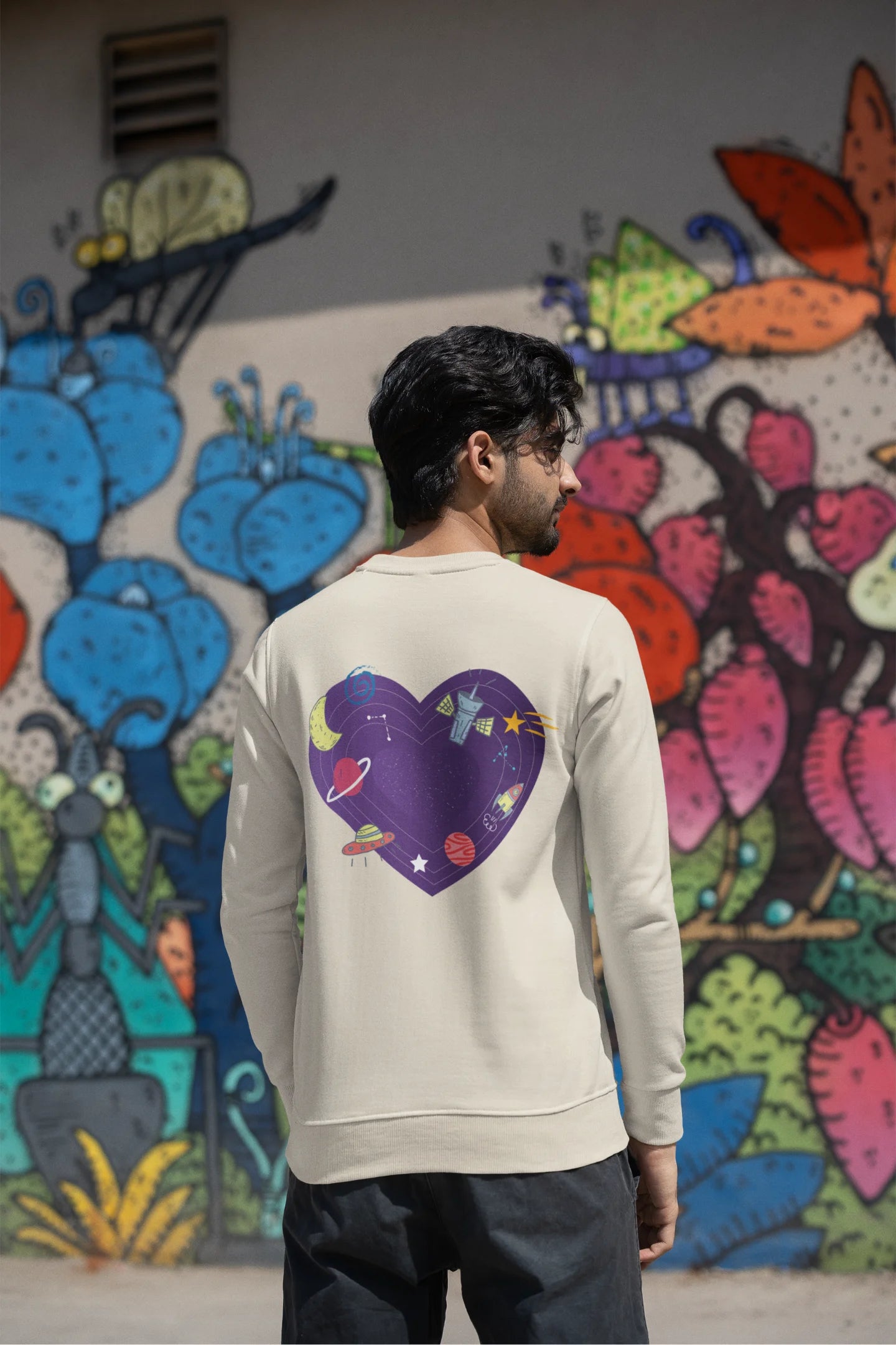 Back view of a male model wearing an cream sweatshirt with the "Paradise" album artwork by Coldplay.