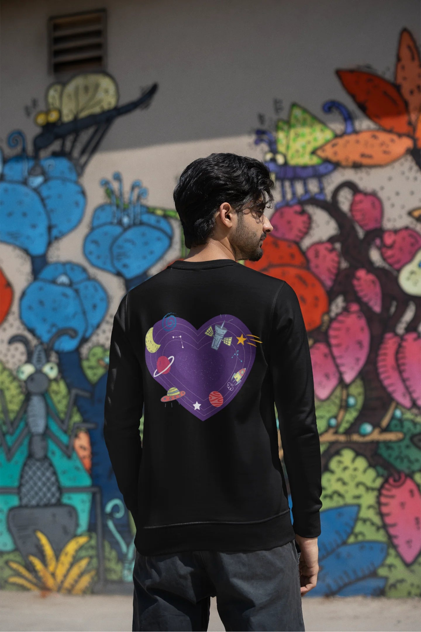 Back view of a male model wearing an black sweatshirt with the "Paradise" album artwork by Coldplay.