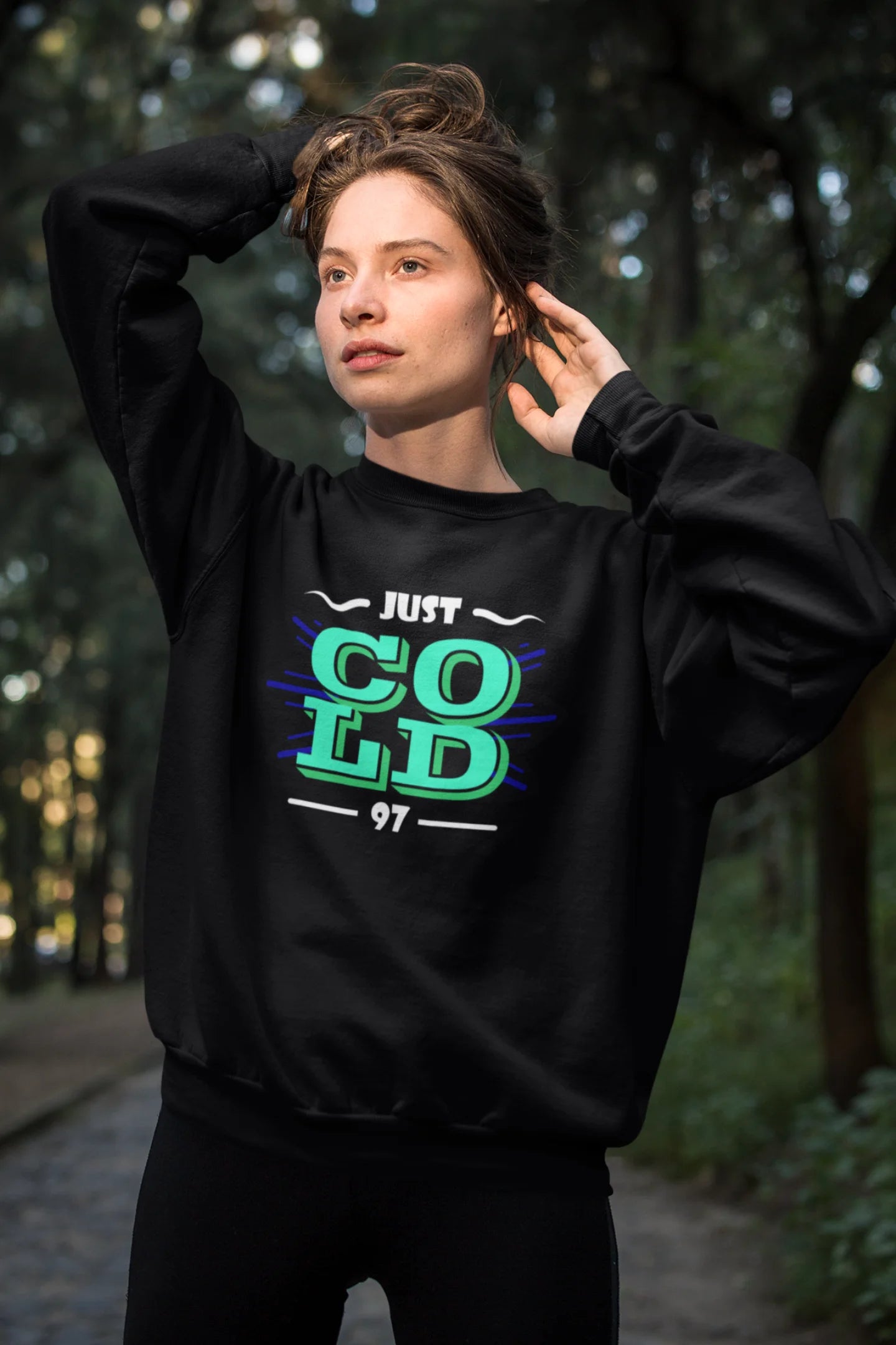 Fourth front view of a female model wearing an black sweatshirt with the text "Just Cold" printed on it.