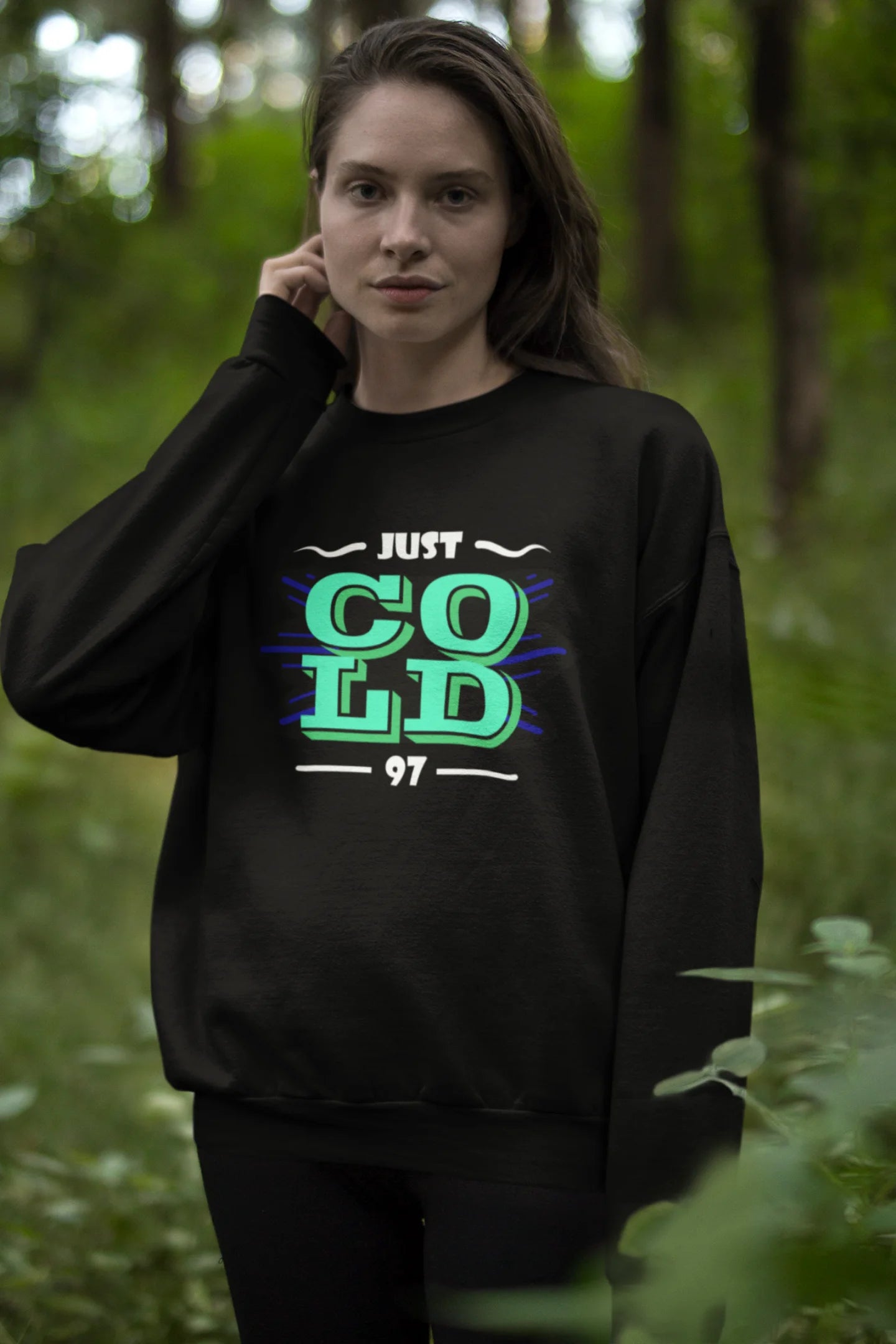 Third front view of a female model wearing an black sweatshirt with the text "Just Cold" printed on it.