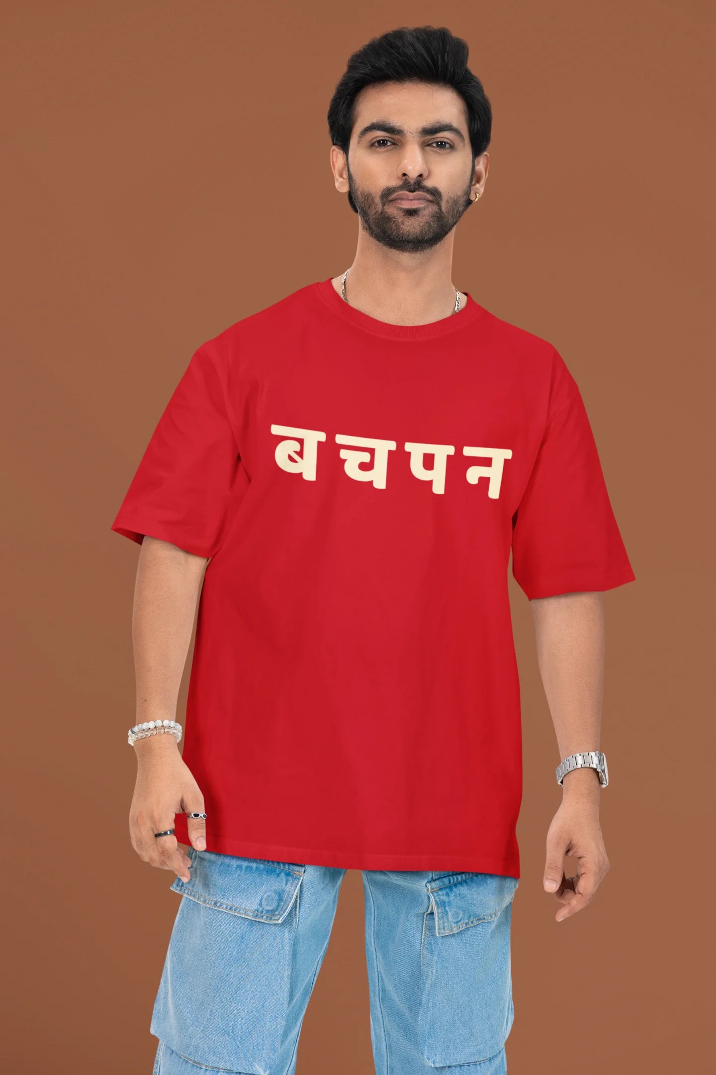 2nd front view of a male model wearing a red oversized t-shirt featuring a collage of illustrations or symbols representing various childhood games commonly played by kids in India.