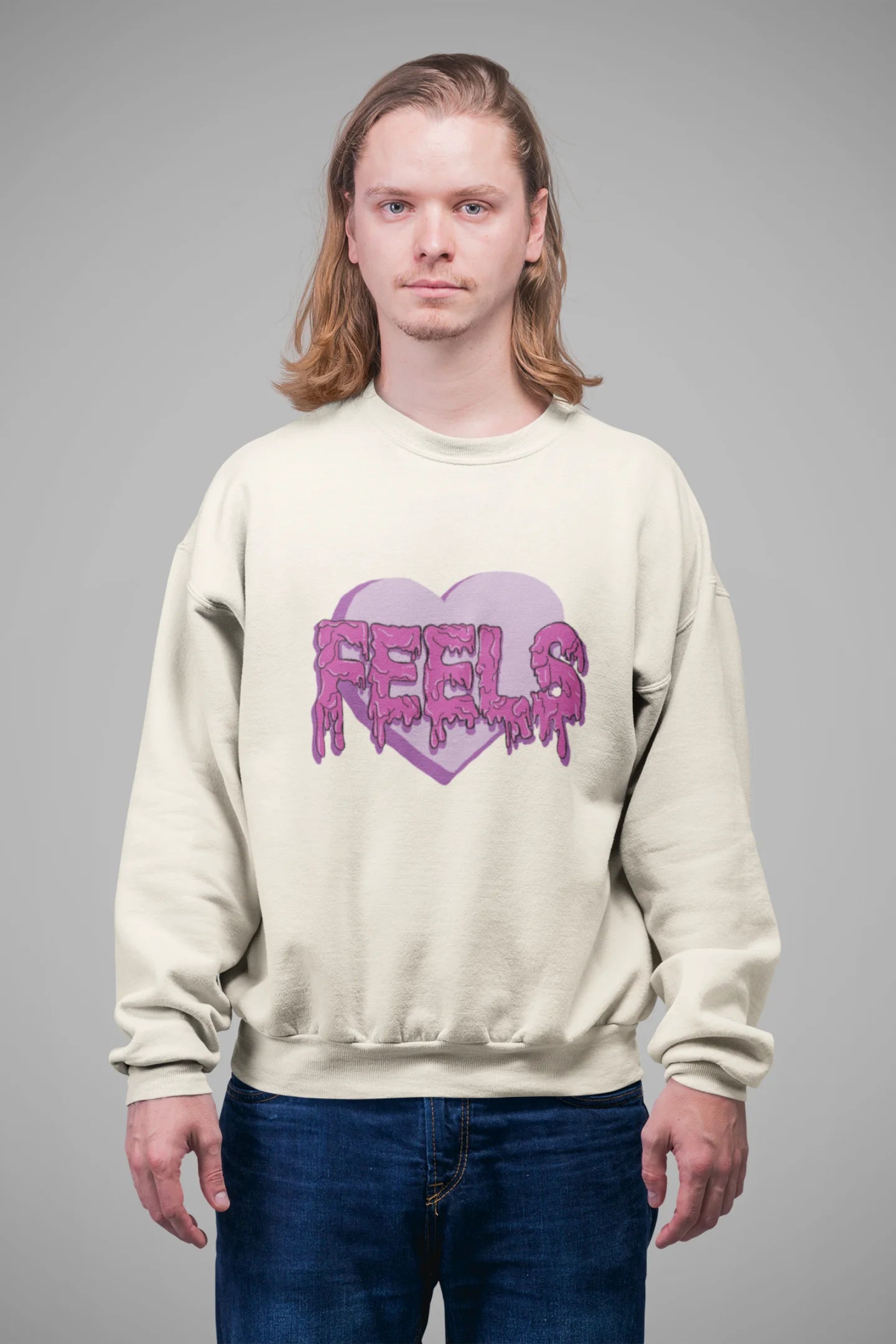 3rd front view of a male model wearing a cream sweatshirt featuring a heart with melting "Feels" text.
