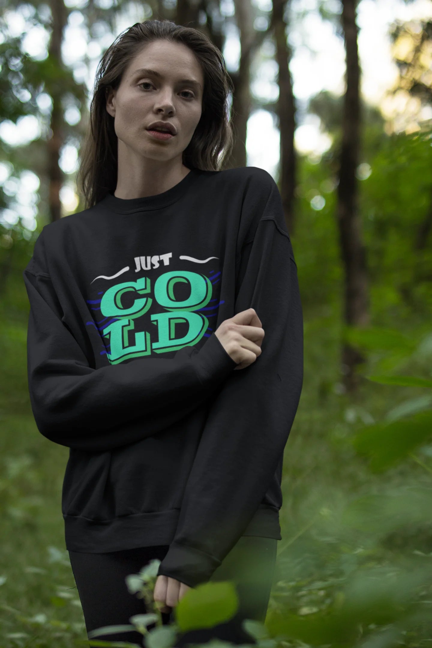 First front view of a female model wearing an black sweatshirt with the text "Just Cold" printed on it.