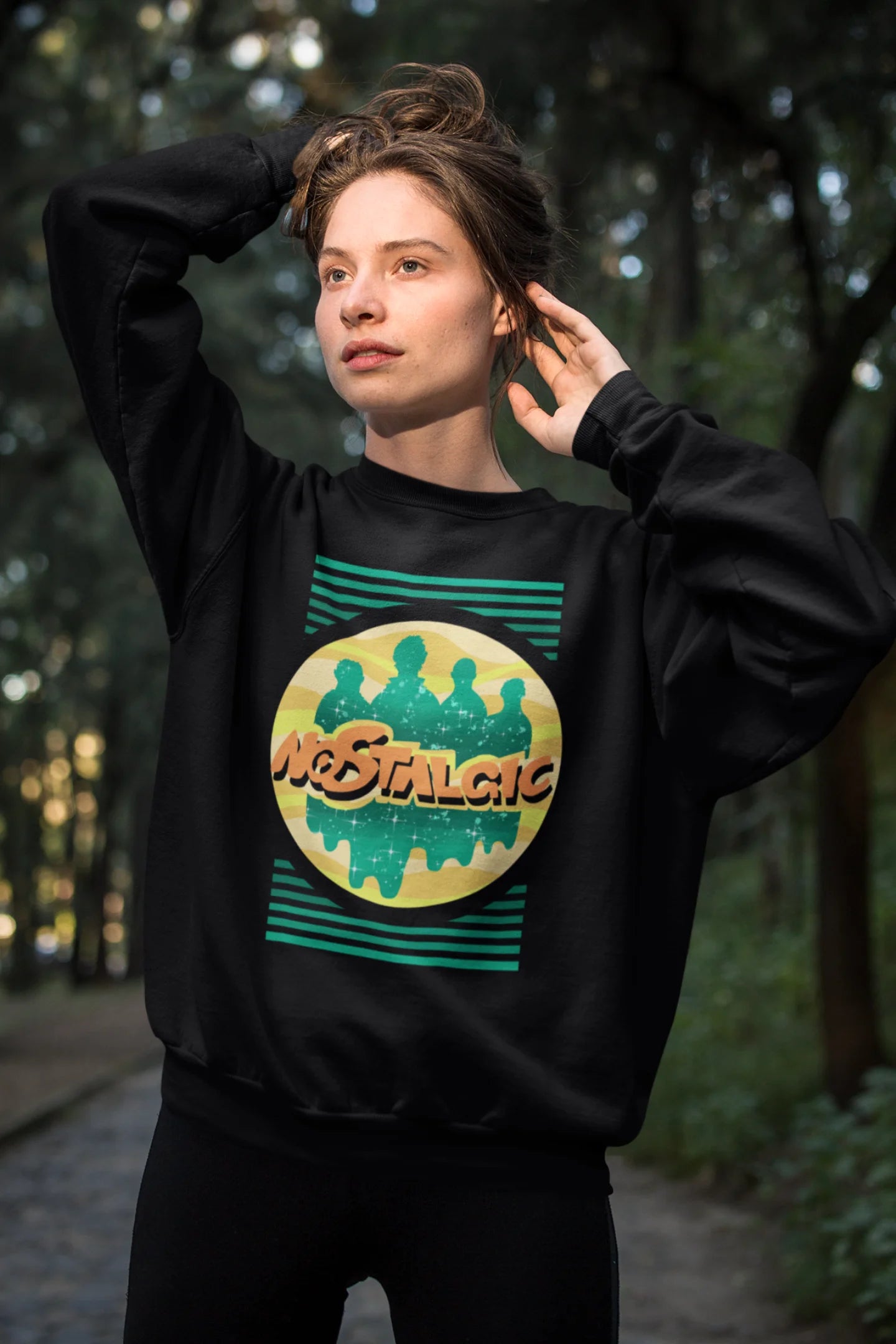 First view of a female model wearing an oversized black sweatshirt with a shadow silhouette of the Coldplay band members and the word "Nostalgic" printed on it.