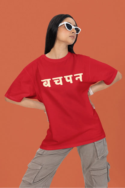 2nd front view of a female model wearing a red oversized t-shirt featuring a collage of illustrations or symbols representing various childhood games commonly played by kids in India.
