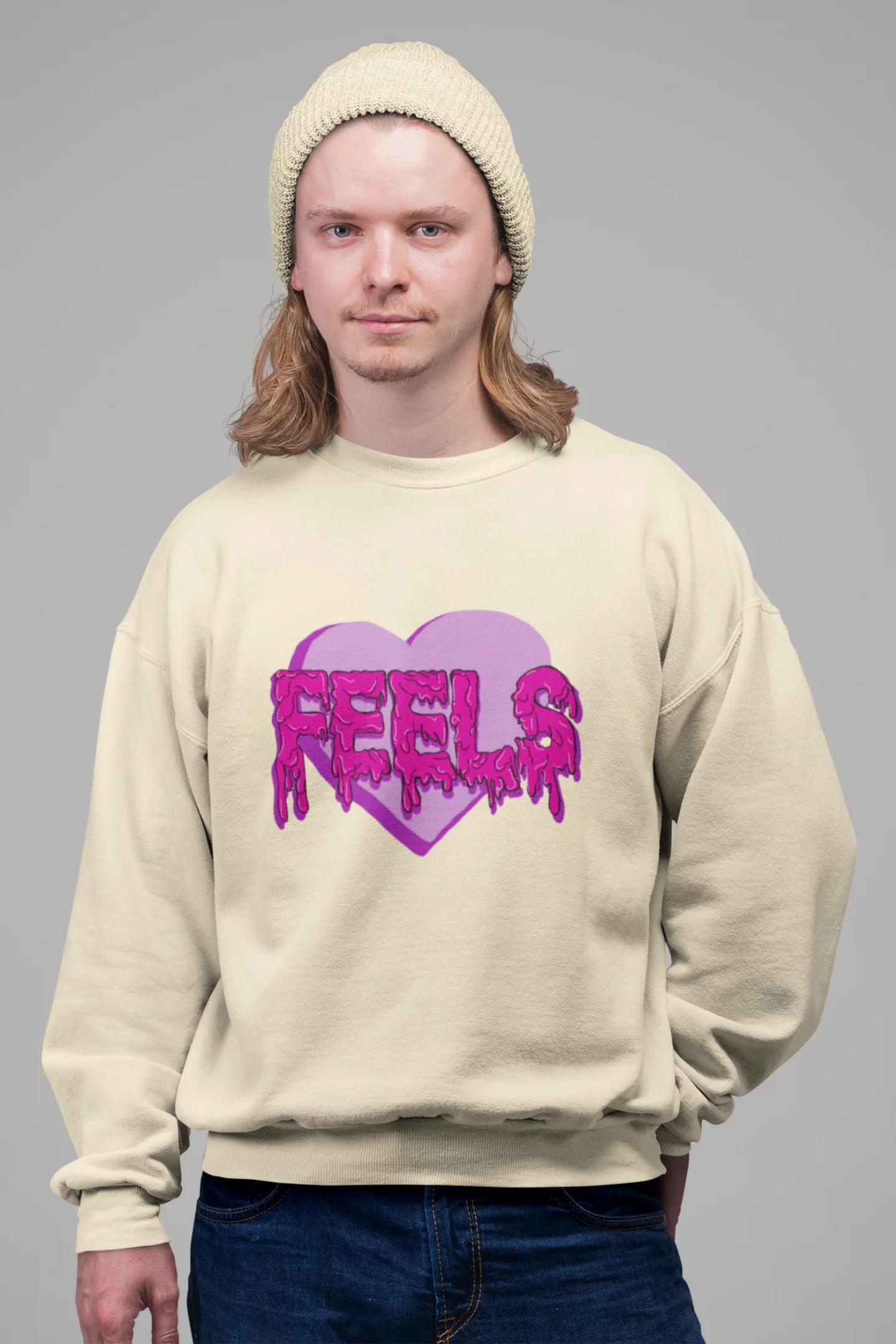4th front view of a male model wearing a cream sweatshirt featuring a heart with melting "Feels" text.