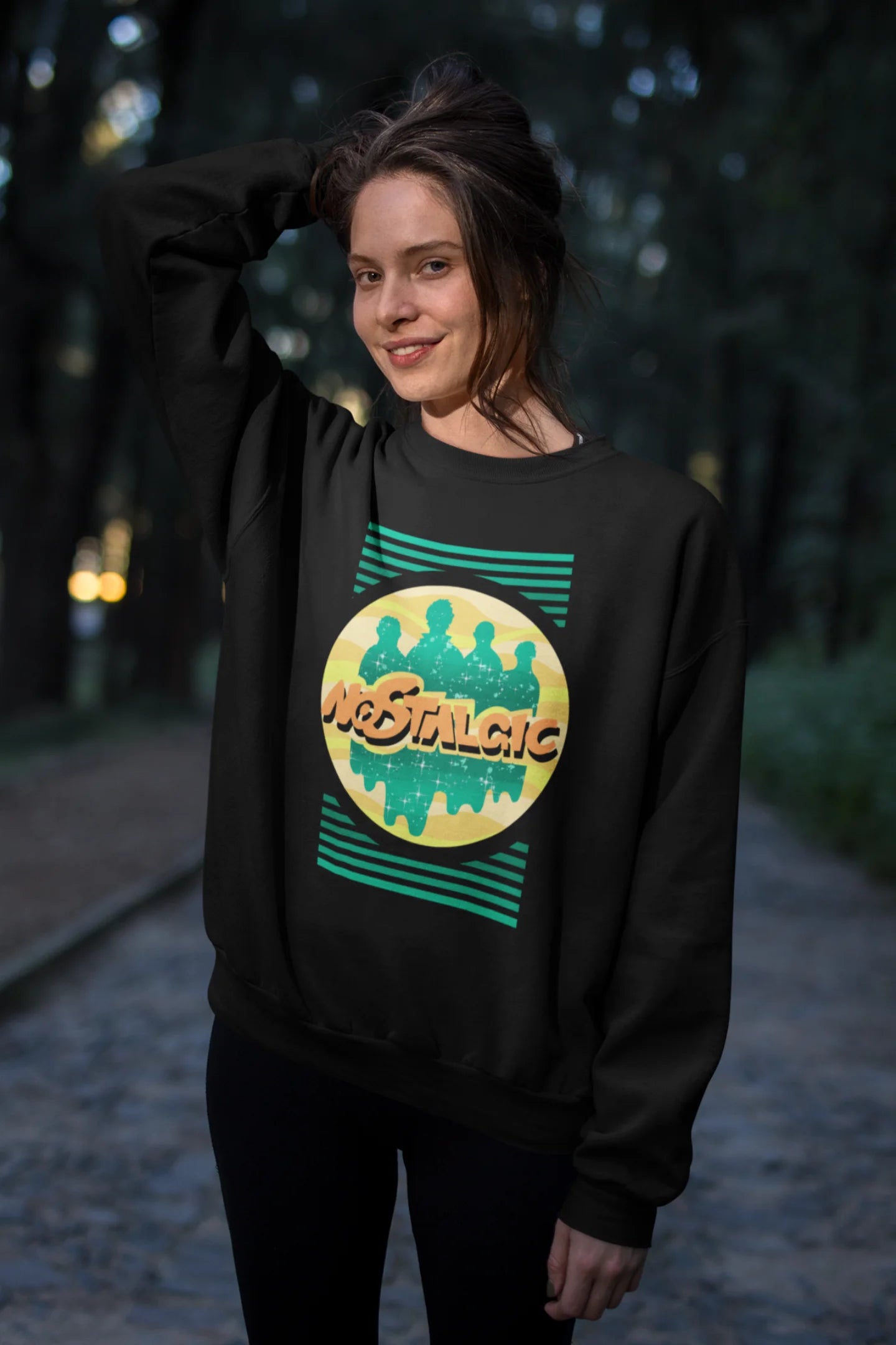 Second view of a female model wearing an oversized black sweatshirt with a shadow silhouette of the Coldplay band members and the word "Nostalgic" printed on it.