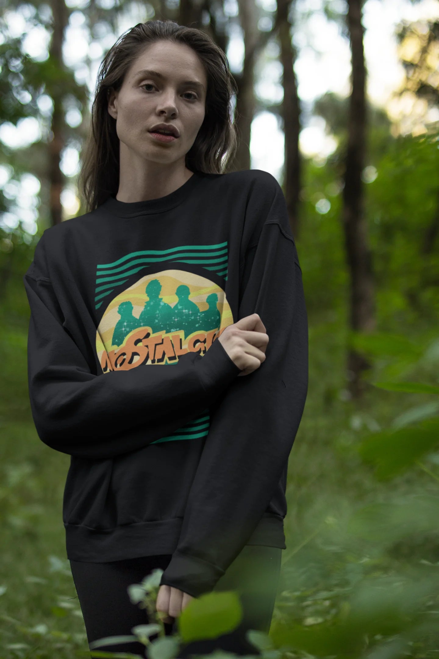Third view of a female model wearing an oversized black sweatshirt with a shadow silhouette of the Coldplay band members and the word "Nostalgic" printed on it.
