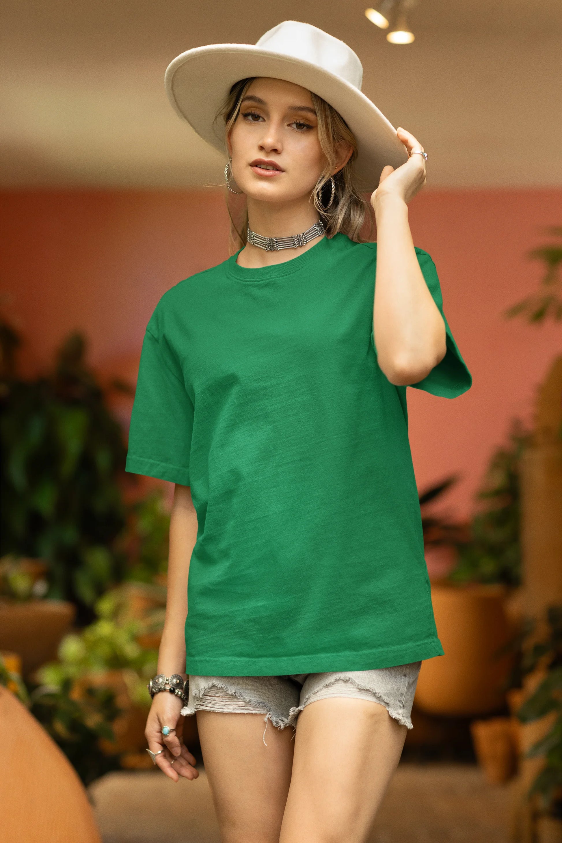 Front view of a male model wearing a forest green oversized tee with a design of a koi fish swimming in a bed of flowers.