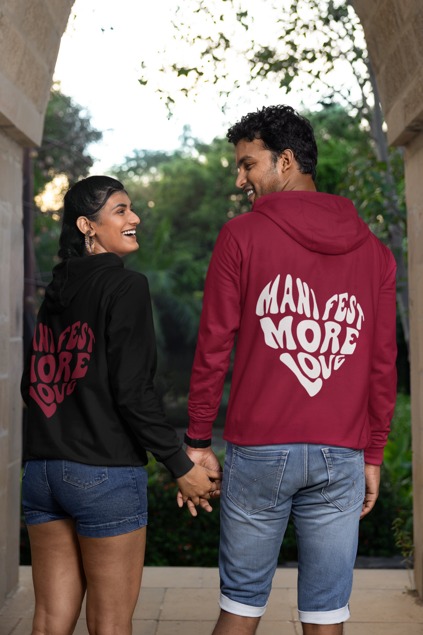 2nd back view of a couple wearing matching hoodies, each with a heart design containing the words "Manifest More Love."