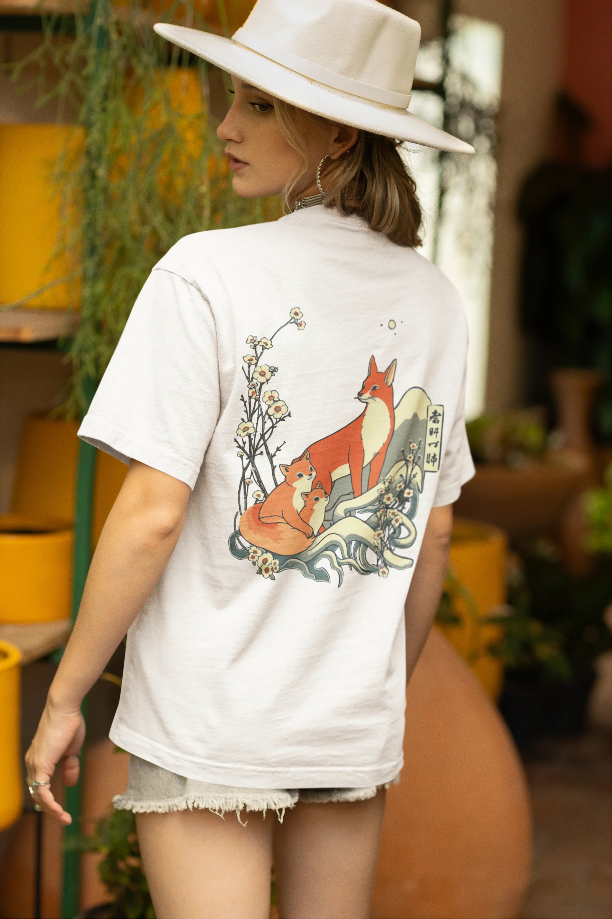 Back view of a female model wearing a off-white oversized tee with a design of a fox and its cub in a traditional Japanese landscape.