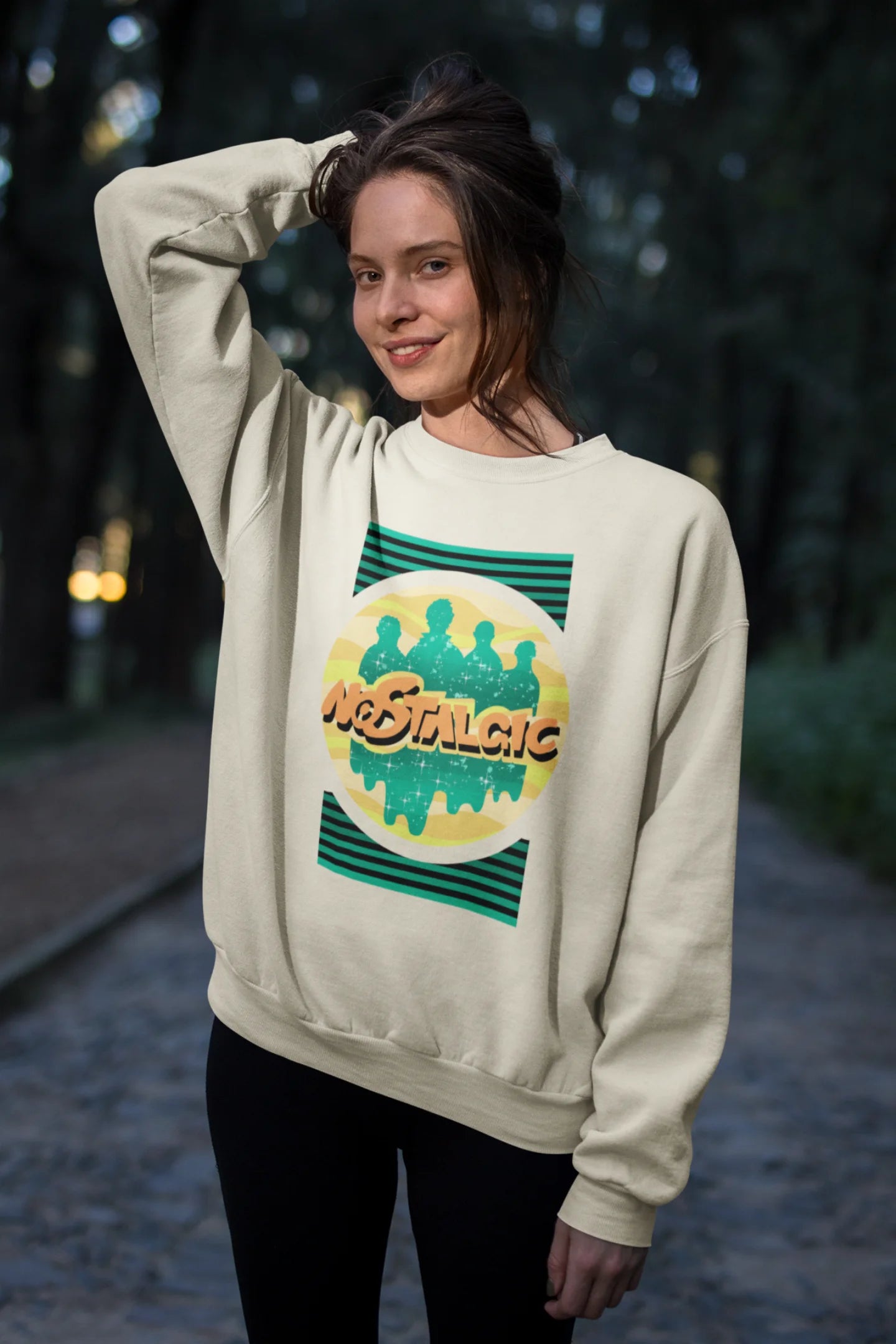 Second view of a female model wearing an oversized cream sweatshirt with a shadow silhouette of the Coldplay band members and the word "Nostalgic" printed on it.