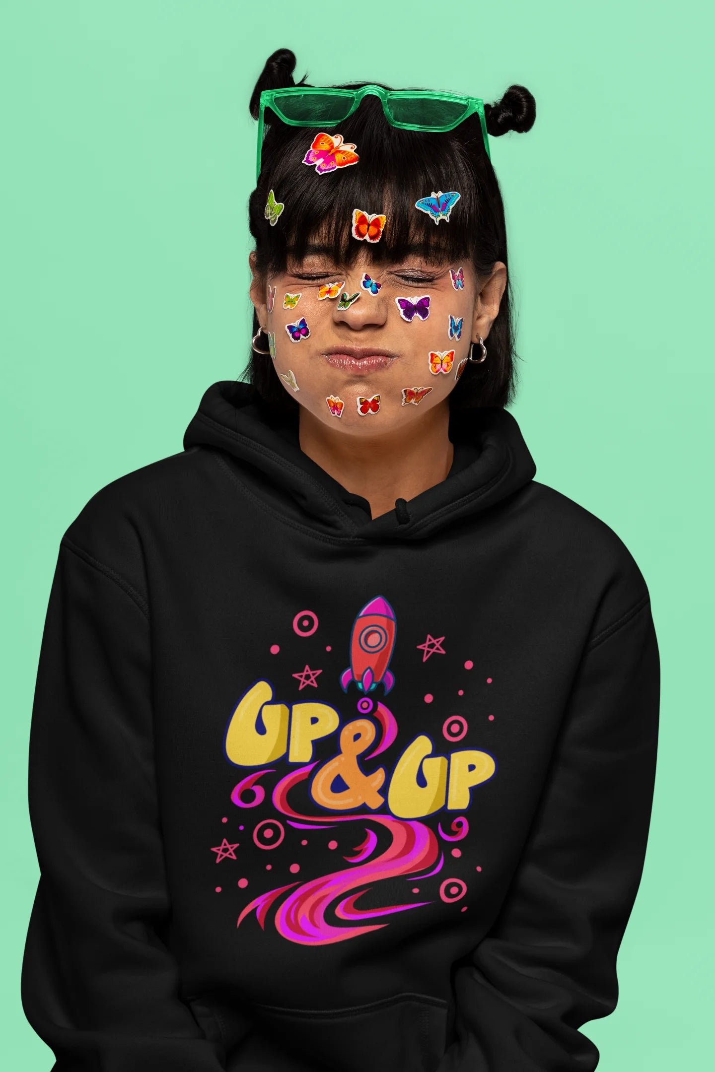 Sixth front view of a female model wearing an black hoodie with a rocket ship design and the text "Up & Up".