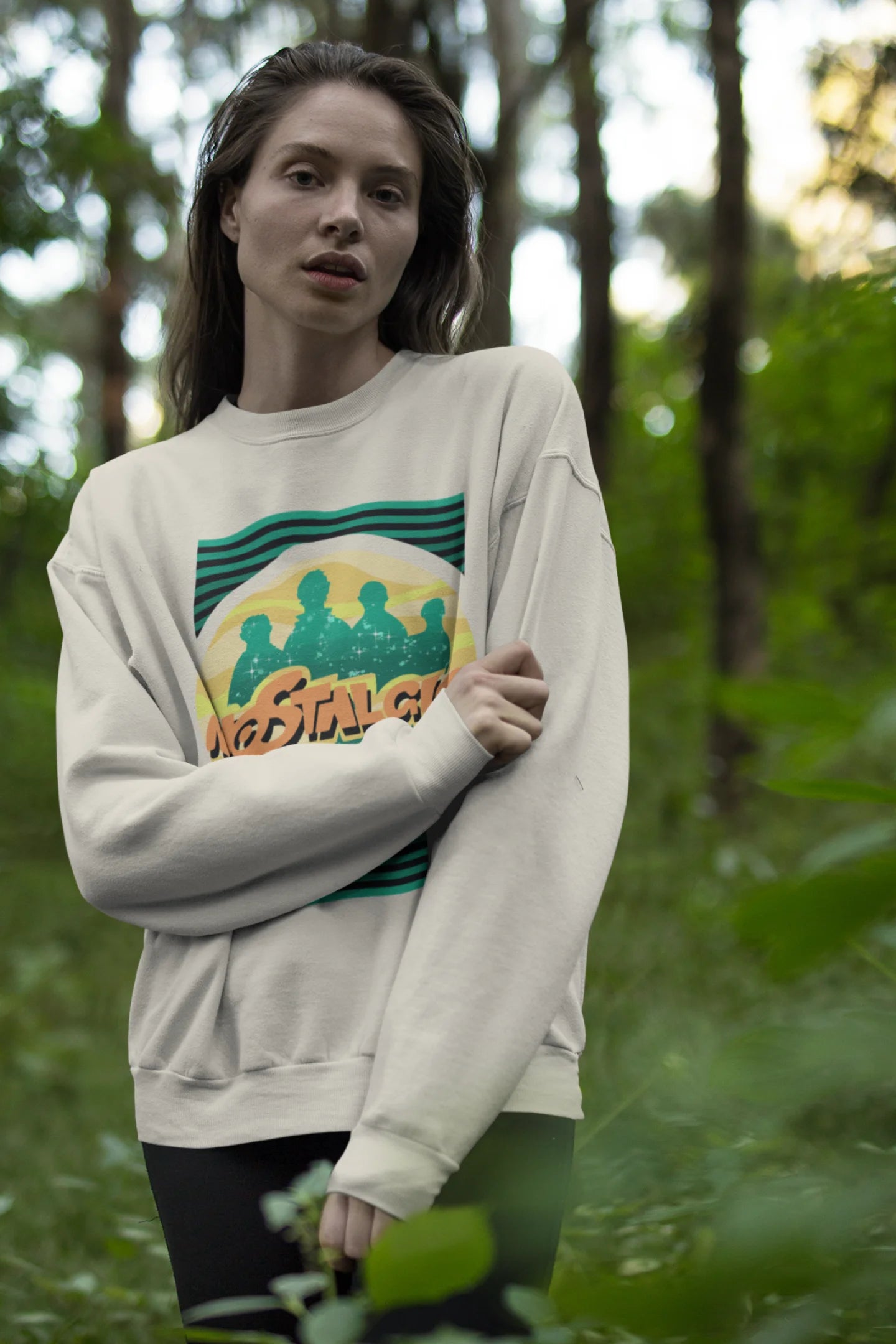 Fourth view of a female model wearing an oversized cream sweatshirt with a shadow silhouette of the Coldplay band members and the word "Nostalgic" printed on it.