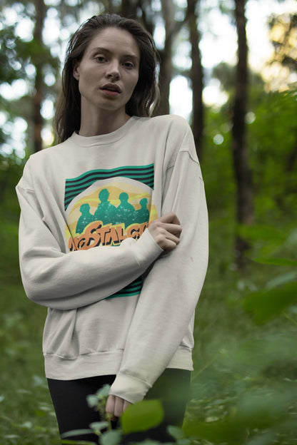 Fourth view of a female model wearing an oversized cream sweatshirt with a shadow silhouette of the Coldplay band members and the word "Nostalgic" printed on it.