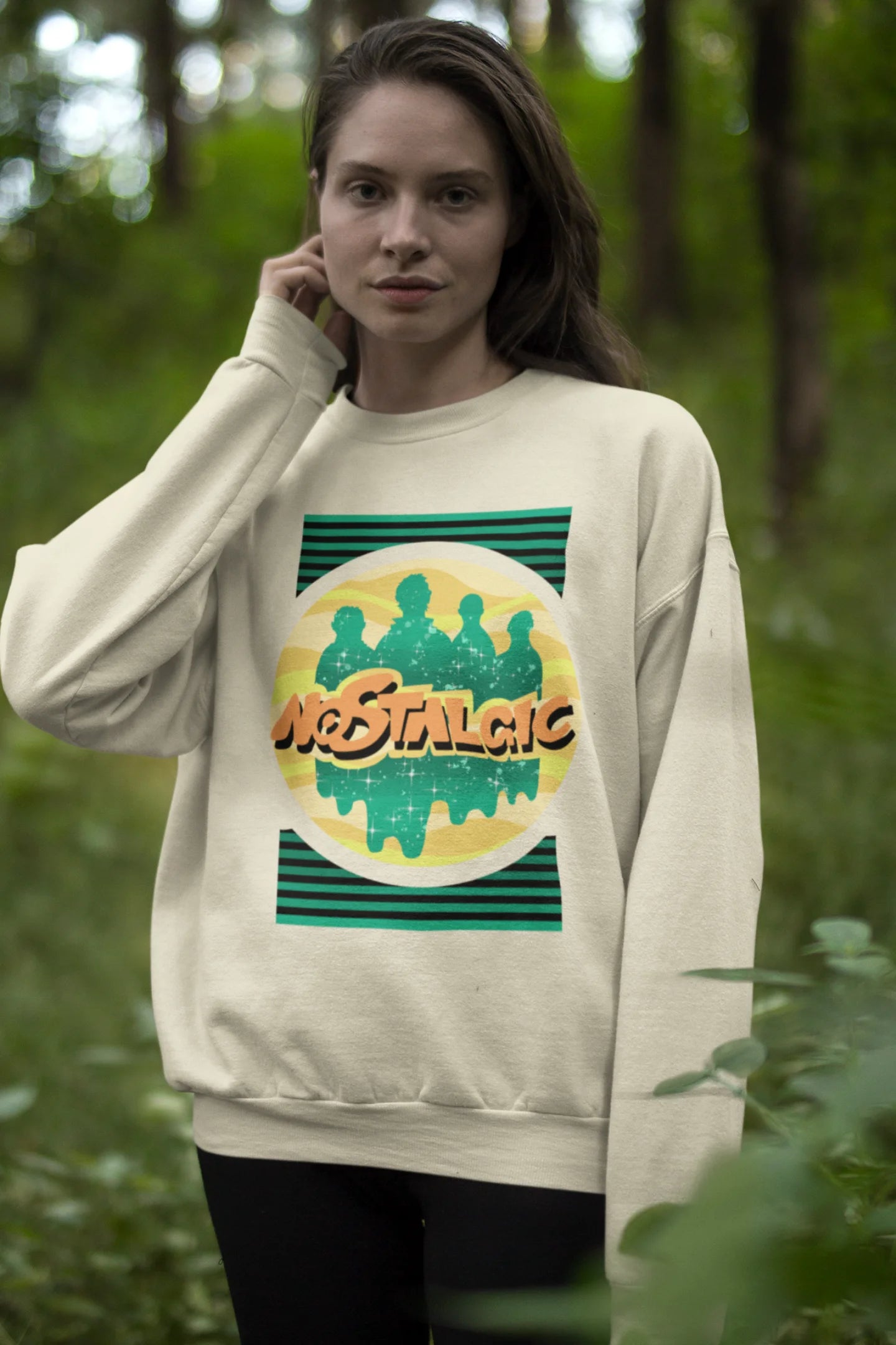 Third view of a female model wearing an oversized cream sweatshirt with a shadow silhouette of the Coldplay band members and the word "Nostalgic" printed on it.