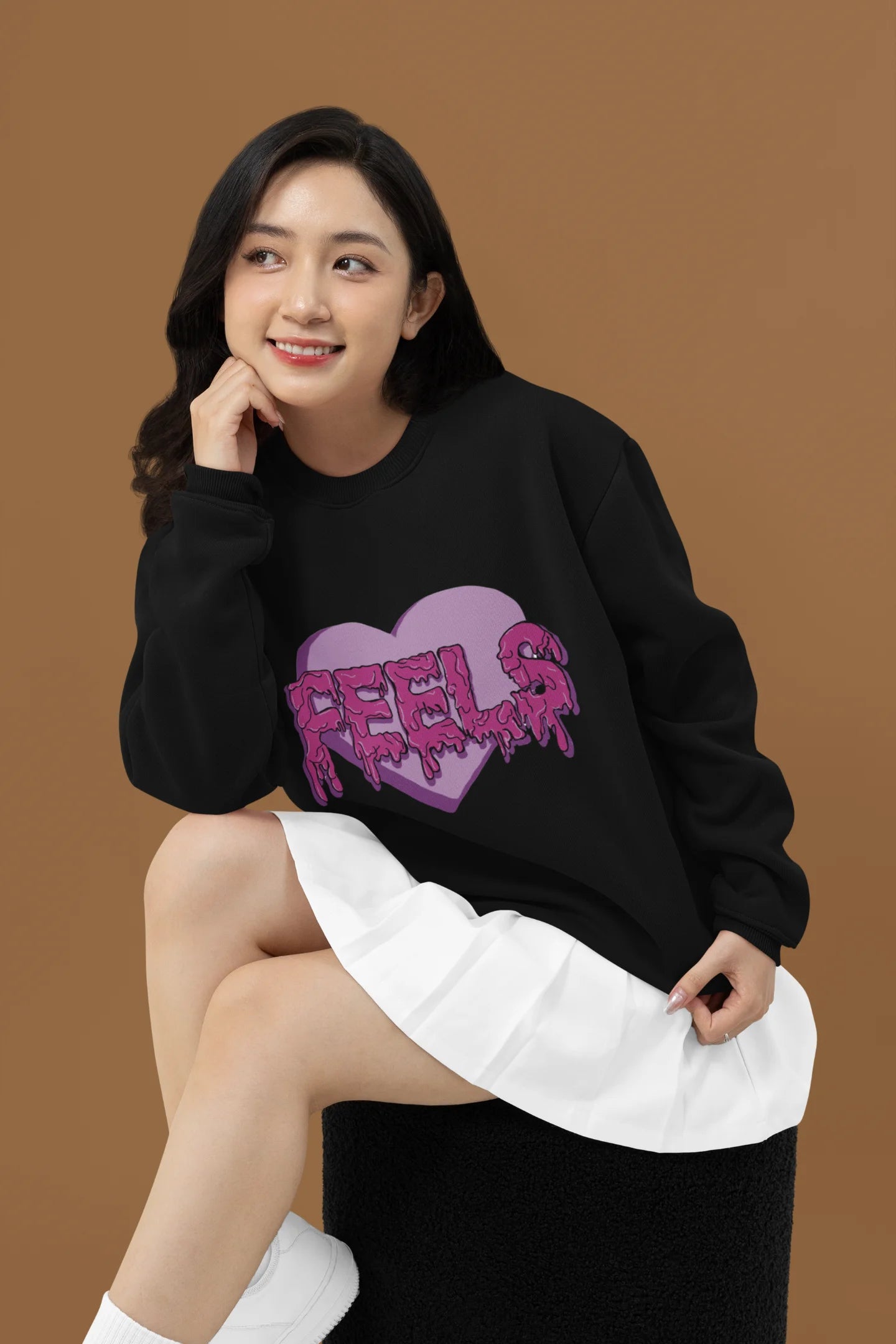 3rd front view of a female model wearing a black sweatshirt featuring a heart with melting "Feels" text.