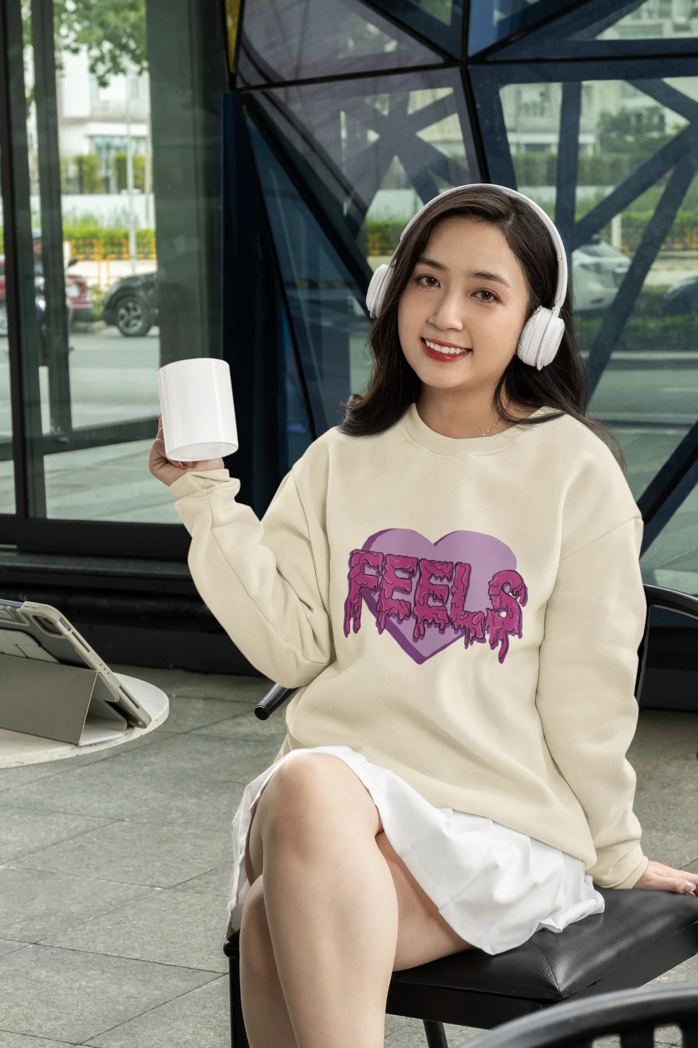 4th front view of a female model wearing a cream sweatshirt featuring a heart with melting "Feels" text.