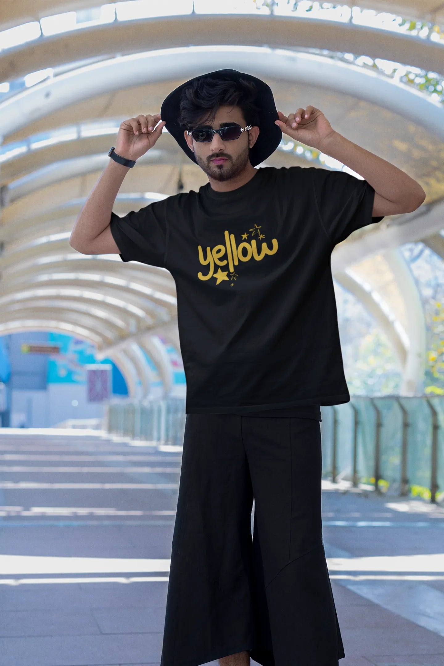 Third front view of a male model wearing a black oversized t-shirt with the "Yellow" album artwork by Coldplay.