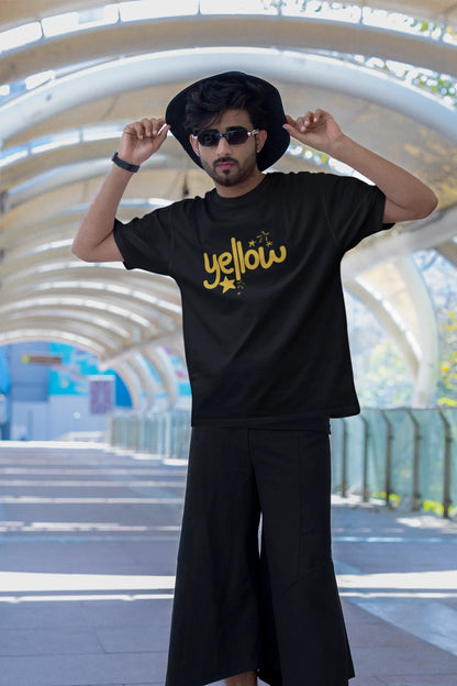 Third front view of a male model wearing a black oversized t-shirt with the "Yellow" album artwork by Coldplay.