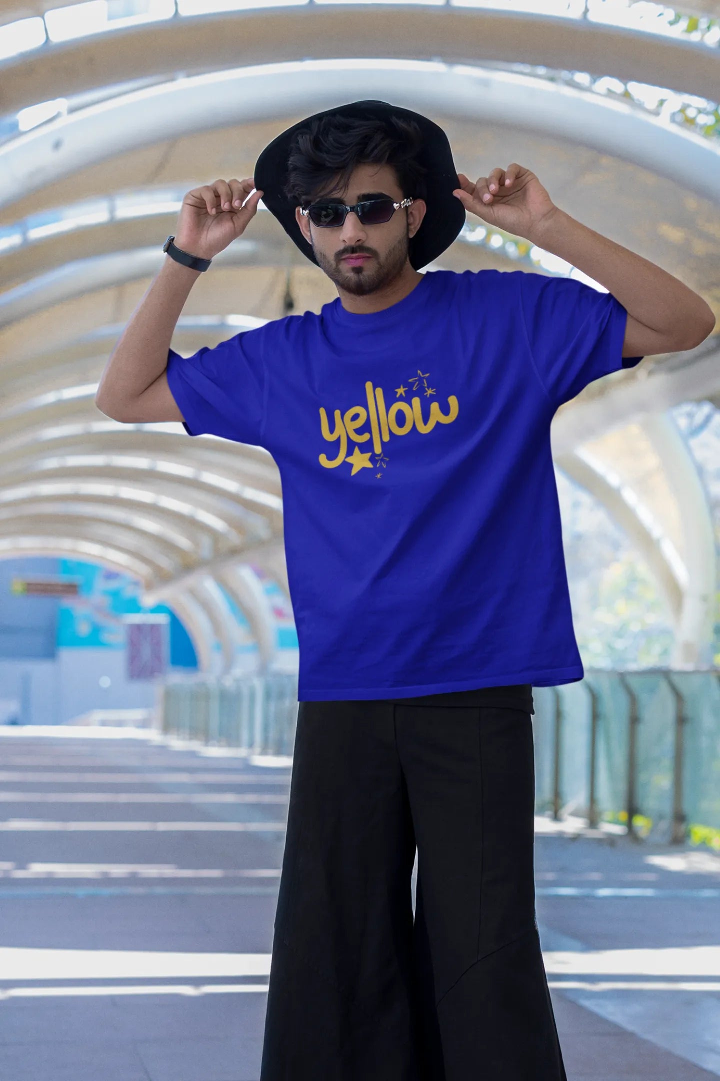 Third front view of a male model wearing a royal blue oversized t-shirt with the "Yellow" album artwork by Coldplay.