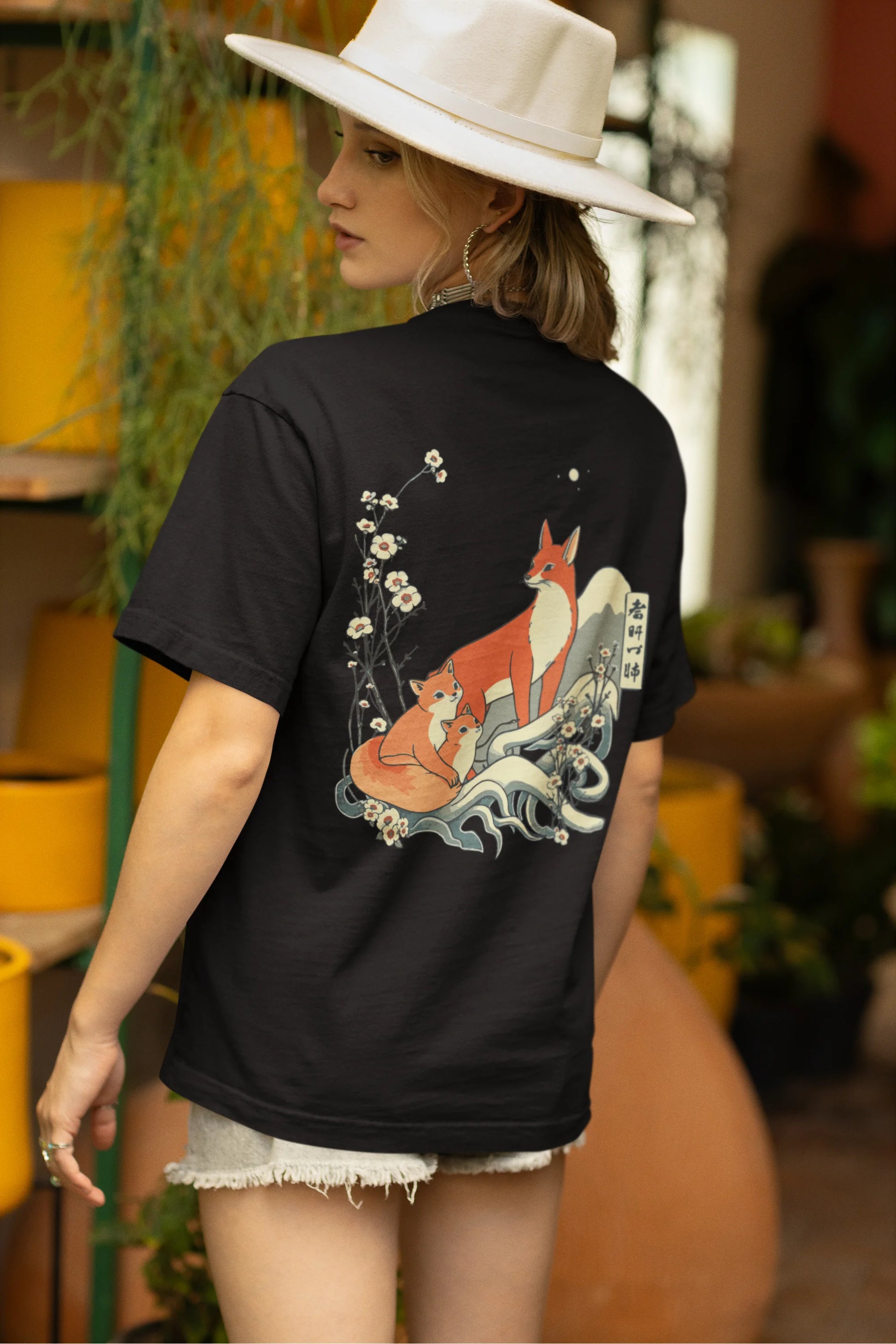 Back view of female model wearing a black oversized tee with a design of a fox and its cub in a traditional Japanese landscape.