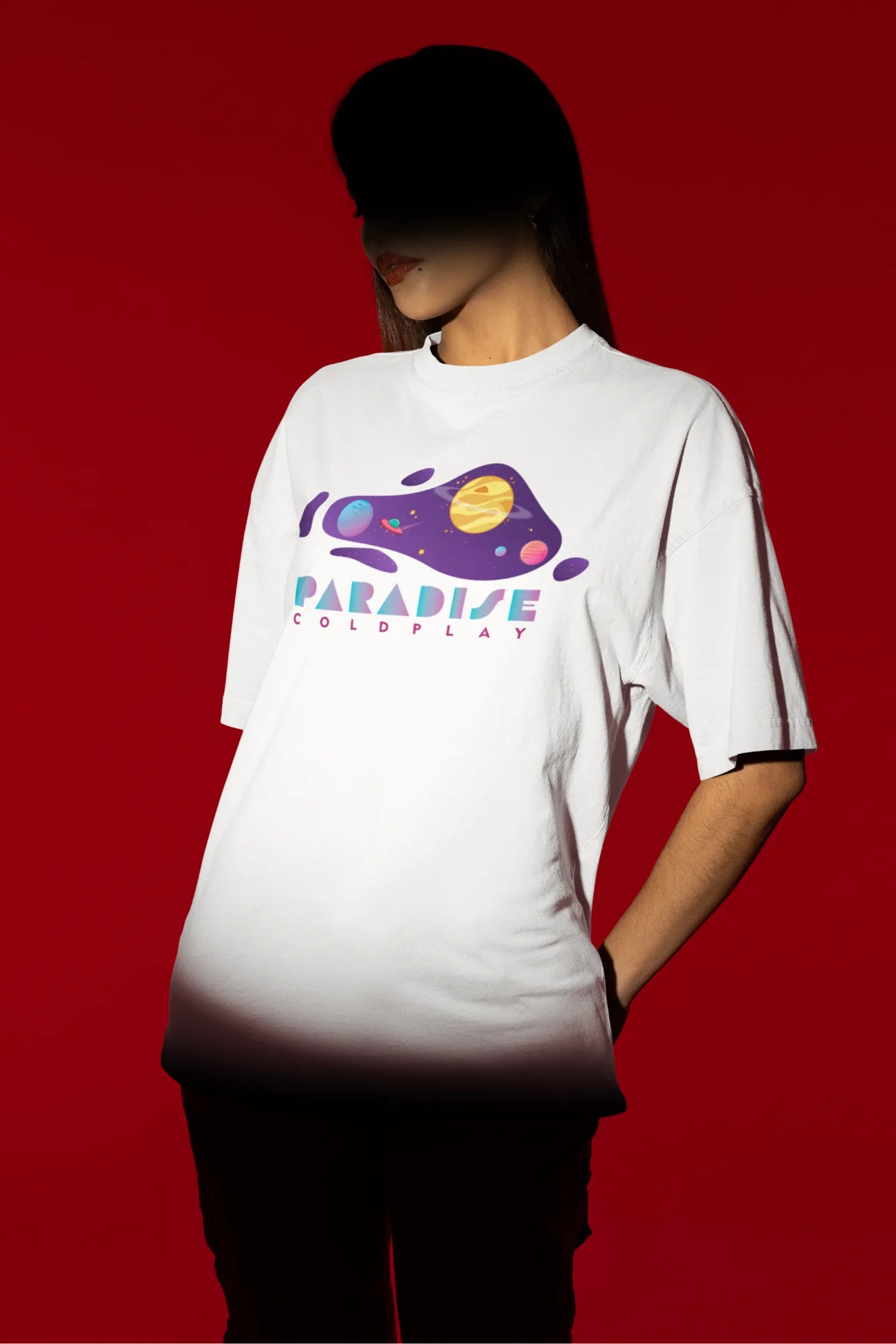 First front view of a female model wearing an white oversized t-shirt with the "Paradise" album artwork by Coldplay.
