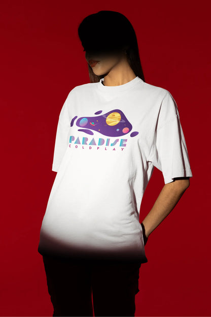 First front view of a female model wearing an white oversized t-shirt with the "Paradise" album artwork by Coldplay.
