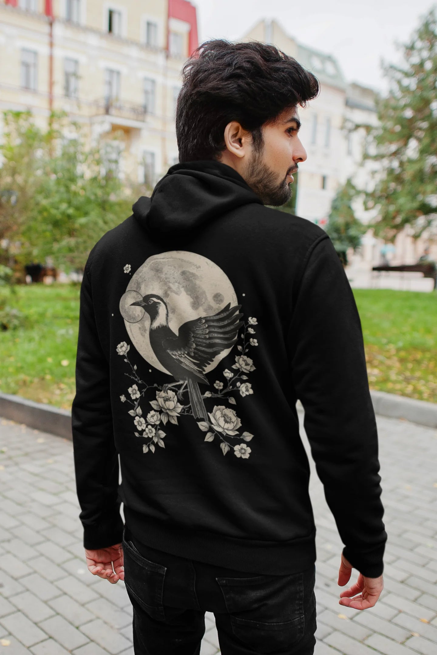 Back view of a male model wearing a black hoodie with a heron taking off under the moonlight.