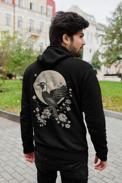 Back view of a male model wearing a black hoodie with a heron taking off under the moonlight.
