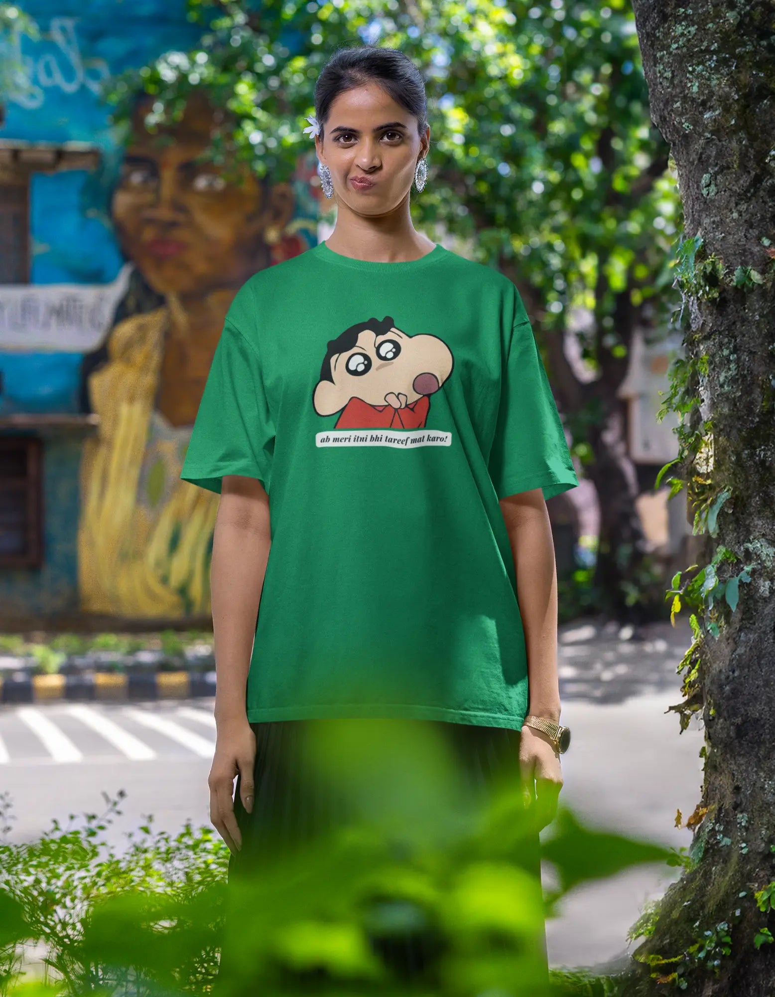 Third front view of female model wearing an oversized forest green tee featuring Shinchan with the text "Don't Praise Me So Much" in Hindi. A perfect blend of humor and nostalgia for Shinchan fans.