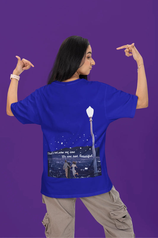 Back view of a female model wearing a royal blue oversized t-shirt featuring a romantic scene of a couple by a lamppost, inspired by Ed Sheeran's "Beautiful People."