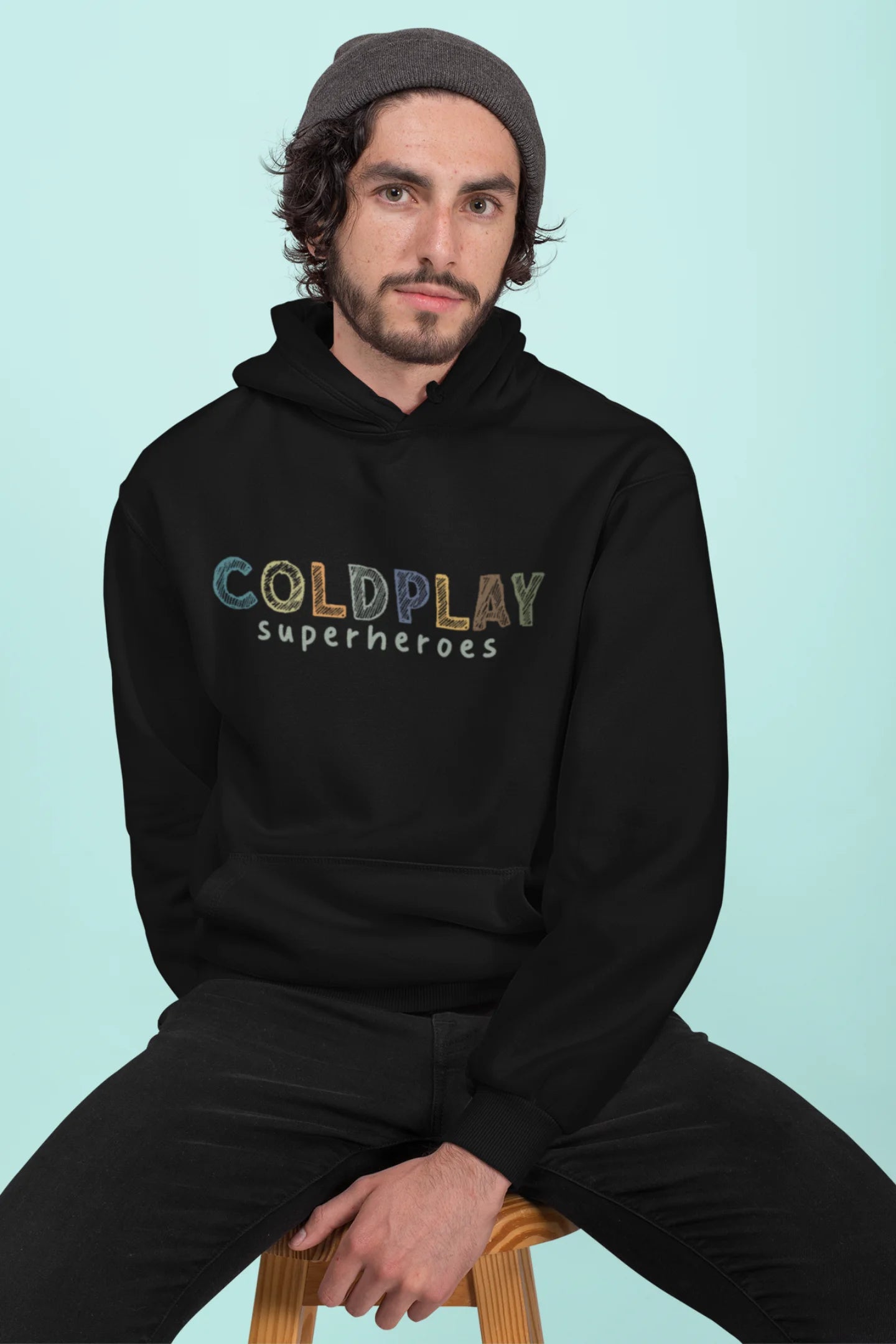 2nd front view of a male model wearing an black hoodie with a design inspired by the "Something Just Like This" music video, featuring the word "Superheroes".