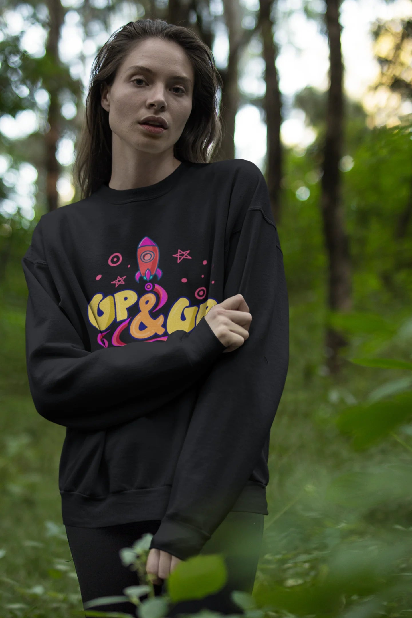 Fourth front view of a female model wearing an black sweatshirt with a rocket ship design and the text "Up & Up".