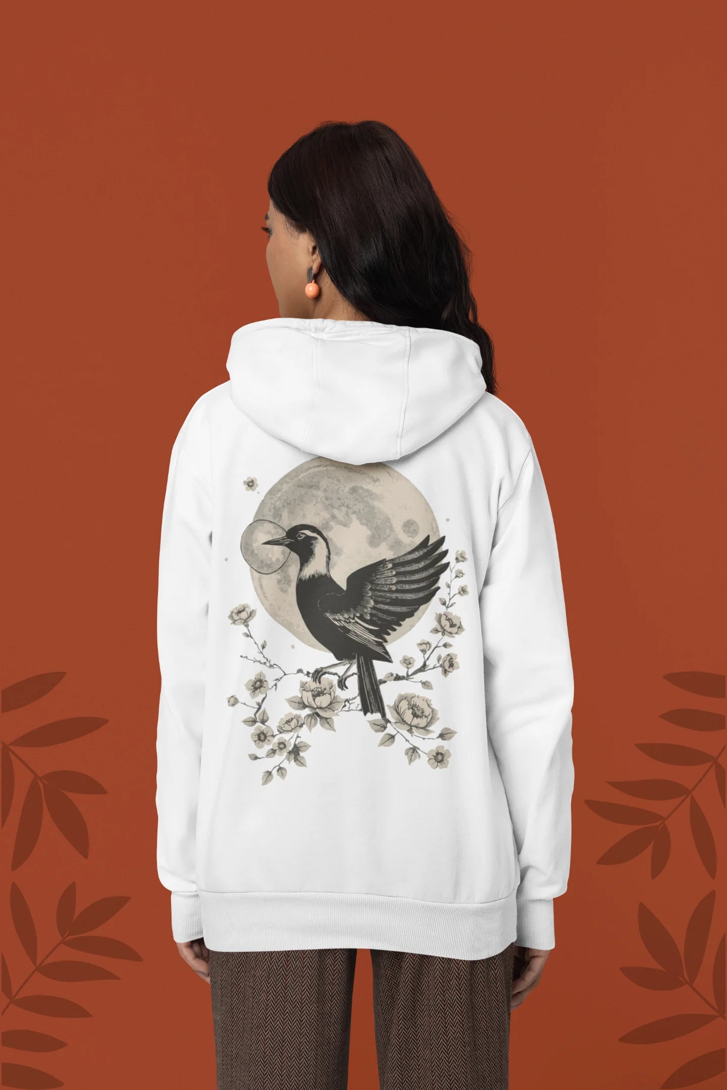 Back view of a female model wearing a white hoodie with a heron taking off under the moonlight.