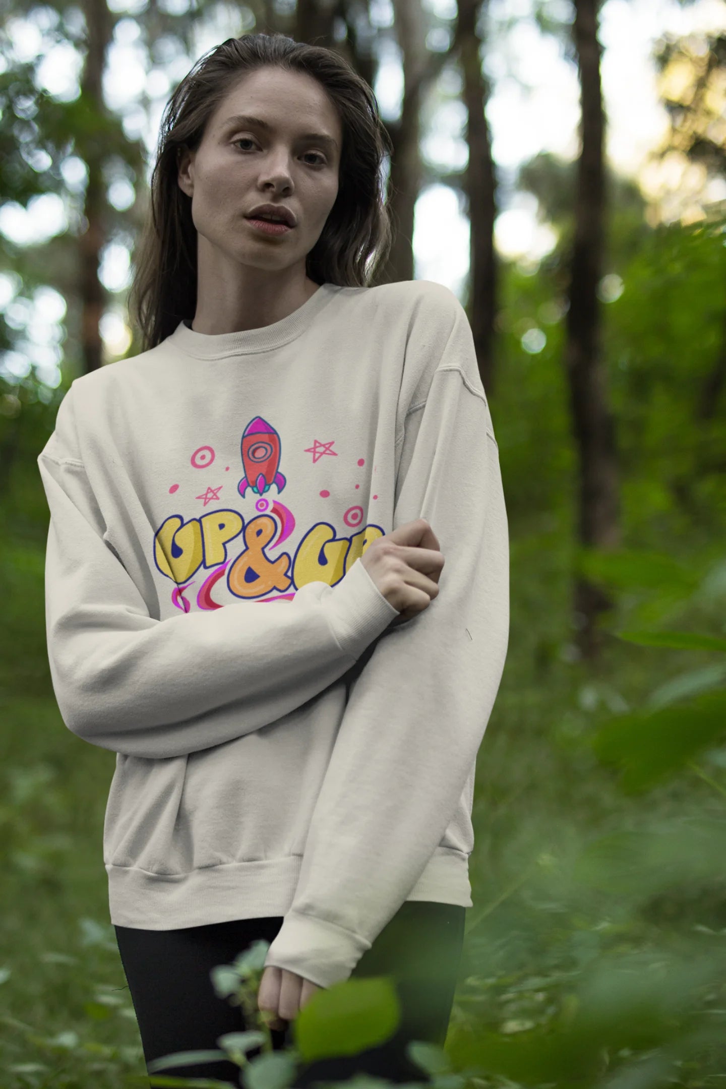 Fourth front view of a male model wearing an cream sweatshirt with a rocket ship design and the text "Up & Up".