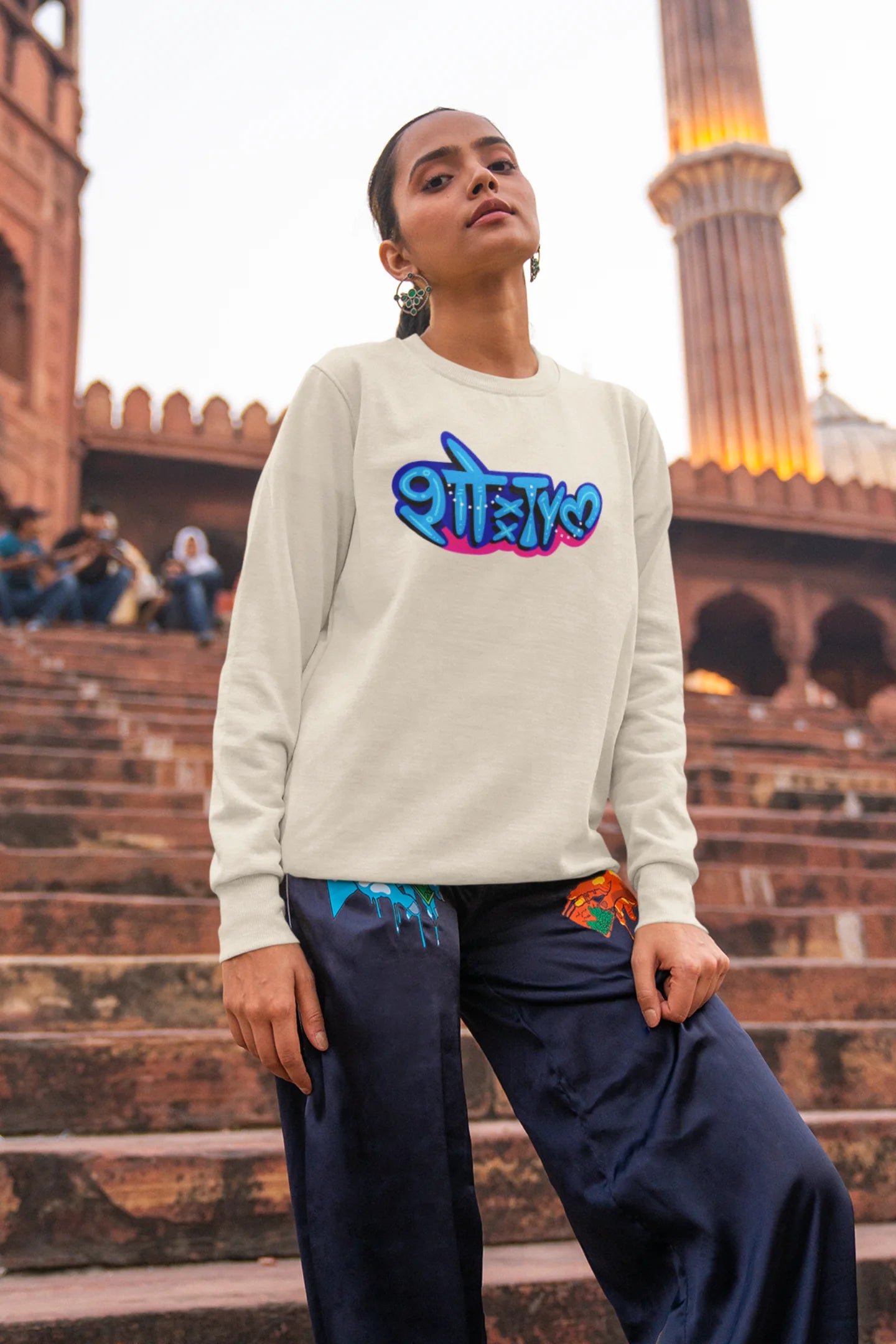 6th front view of a female model wearing a cream oversized t-shirt featuring "Showtime" in Hindi.
