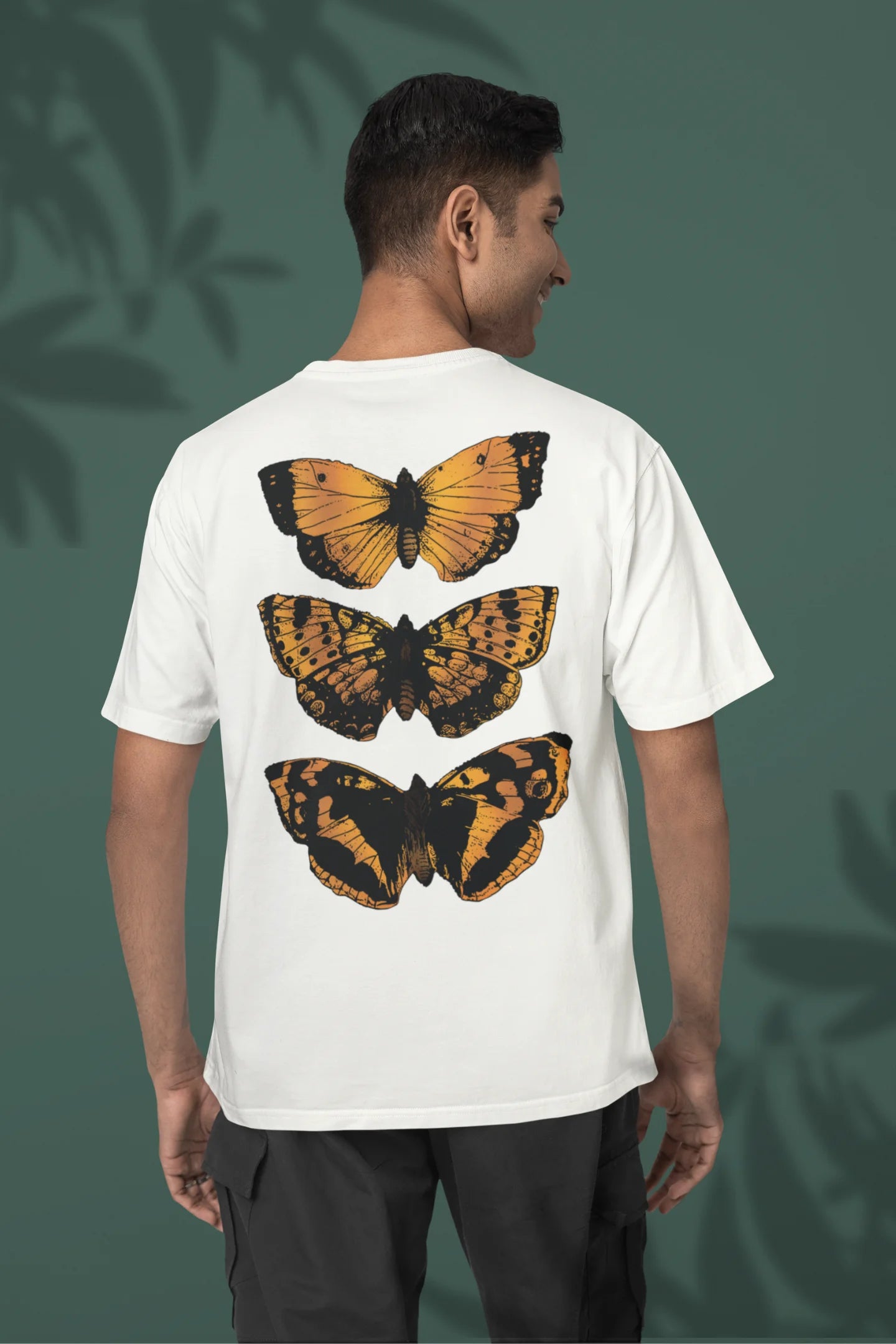 Back view of a male model wearing a off-white oversized tee with a design featuring three different types of butterflies, symbolizing the beauty and diversity of nature.