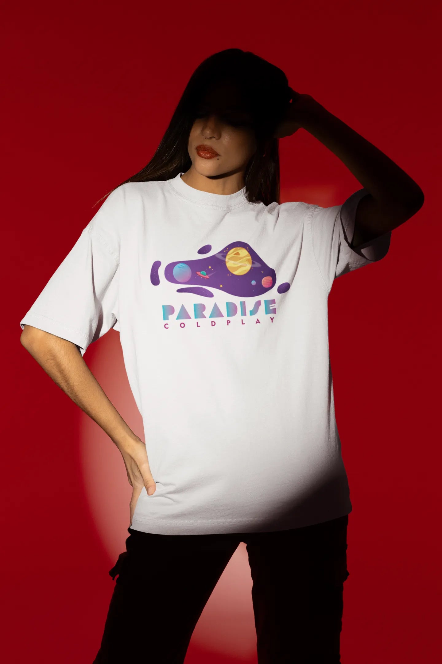 Fourth front view of a female model wearing an white oversized t-shirt with the "Paradise" album artwork by Coldplay.
