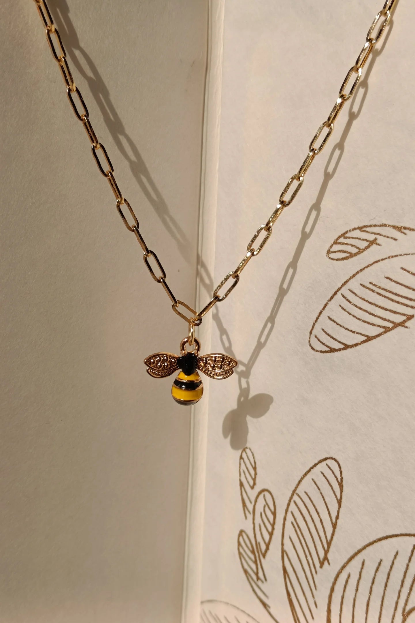 3rd view of a gold chain necklace with a small pendant shaped like a honey bee.