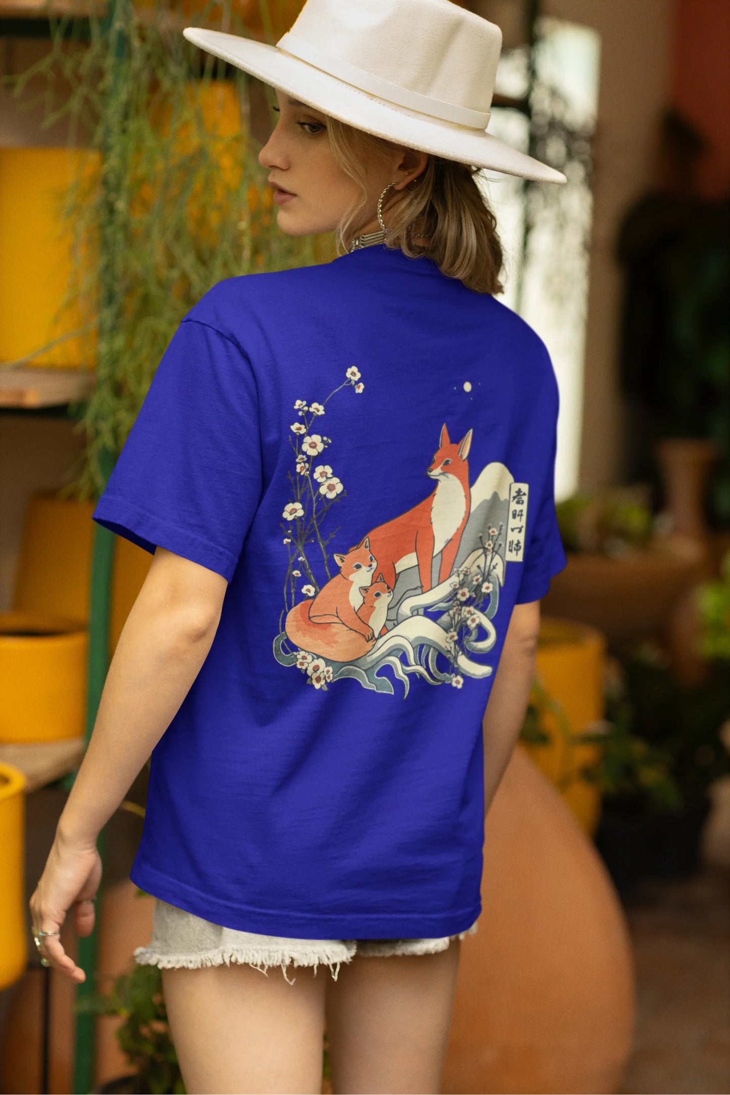 Back view of a female model wearing a royal blue oversized tee with a design of a fox and its cub in a traditional Japanese landscape.
