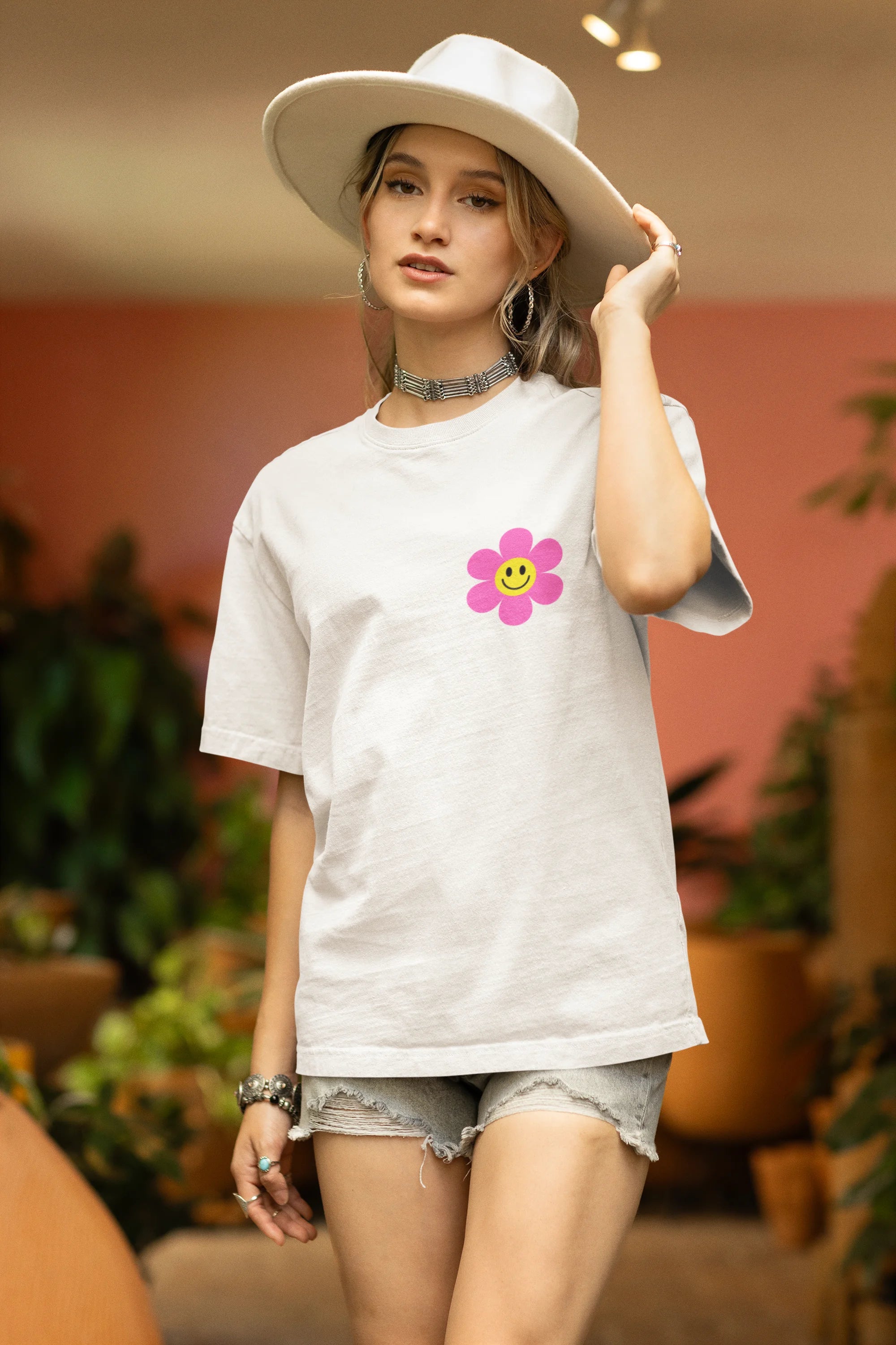 Side view of a female model wearing an oversized off-white t-shirt with a positive message "Keep Smiling" surrounded by colorful flowers and a smiley face emoji. Ideal for those who love cheerful clothing and spreading positivity.