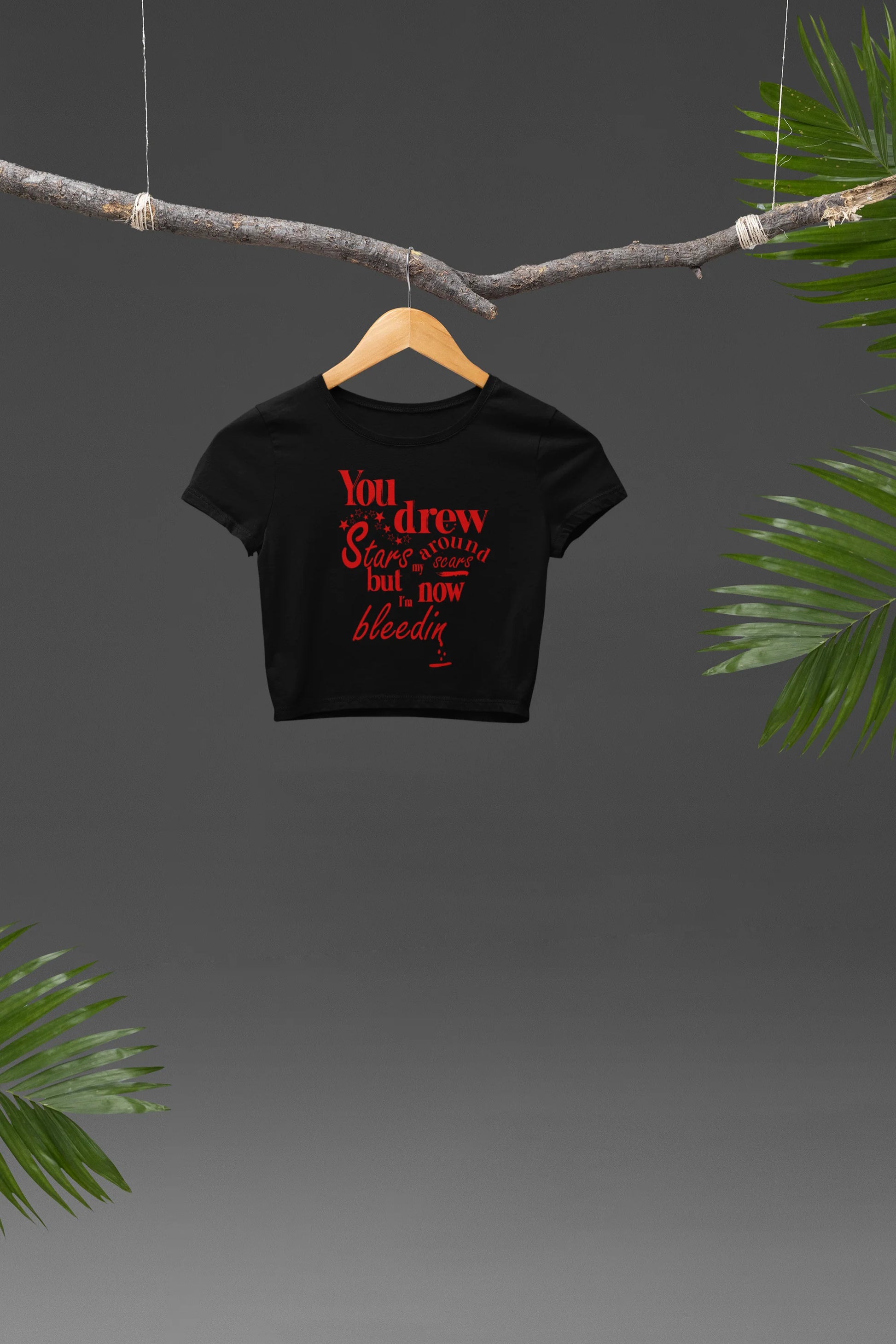 Front view of a black crop top featuring the lyrics "You drew stars around my scars but now I'm bleeding," perfect for Swiftie fans.