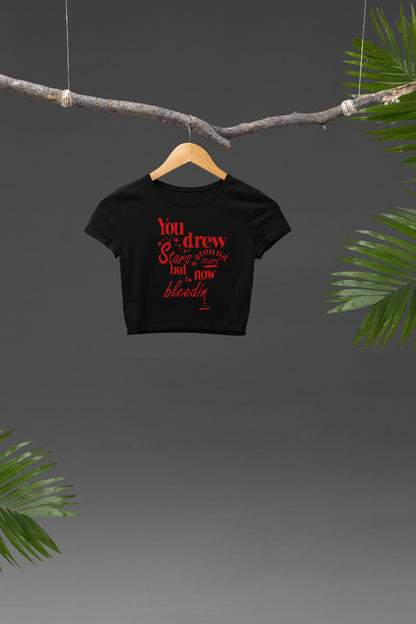 Front view of a black crop top featuring the lyrics "You drew stars around my scars but now I'm bleeding," perfect for Swiftie fans.