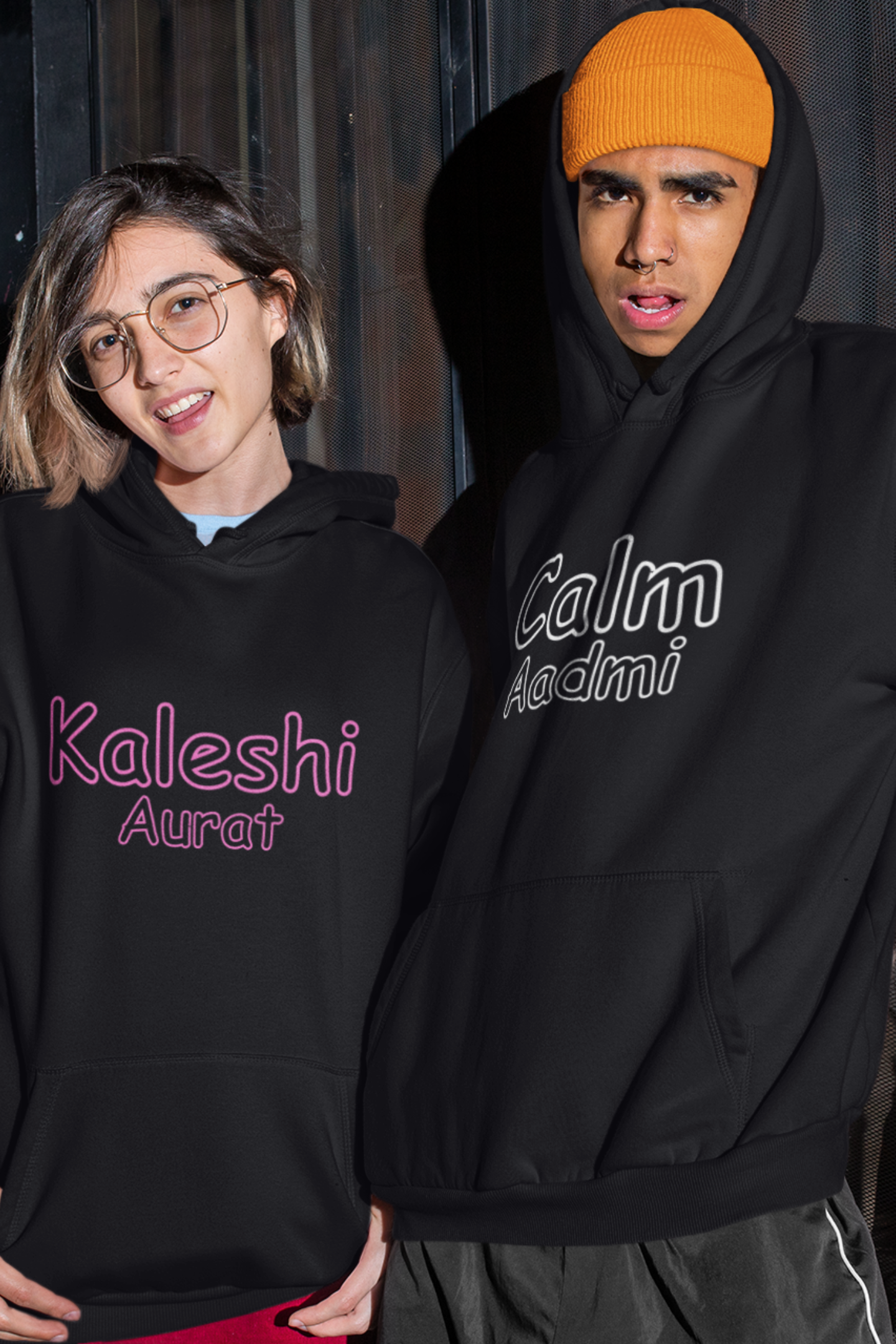 A smiling couple wearing matching hoodies, one with "Calm one" and the other with "Chaotic one" printed on them in Hindi.