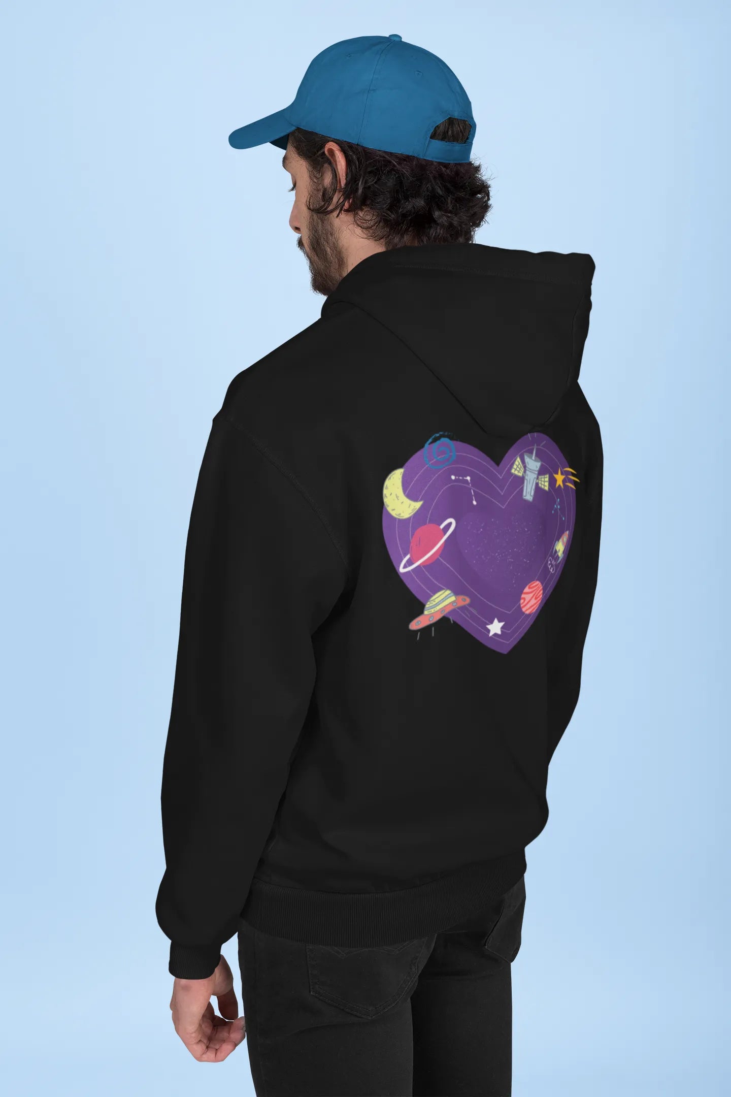 Back view of a male model wearing an black hoodie with the "Paradise" album artwork by Coldplay.